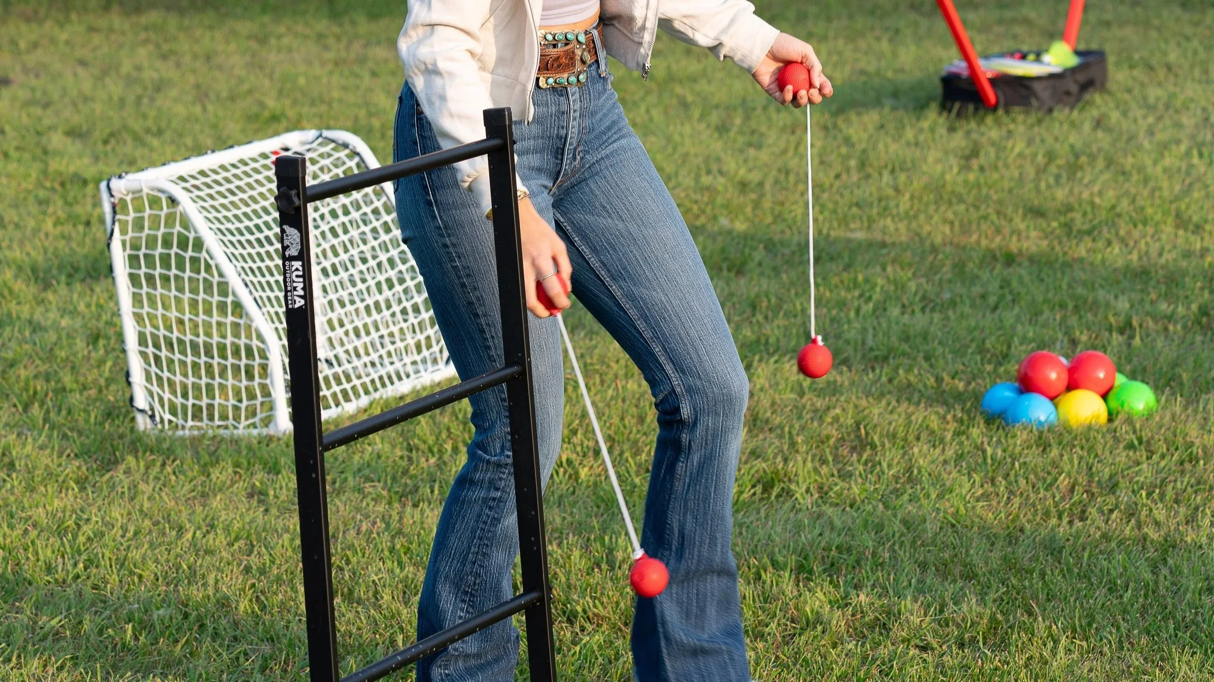 Person playing croquet on a grassy field, with colorful balls arranged in a pyramid shape and small goals nearby.