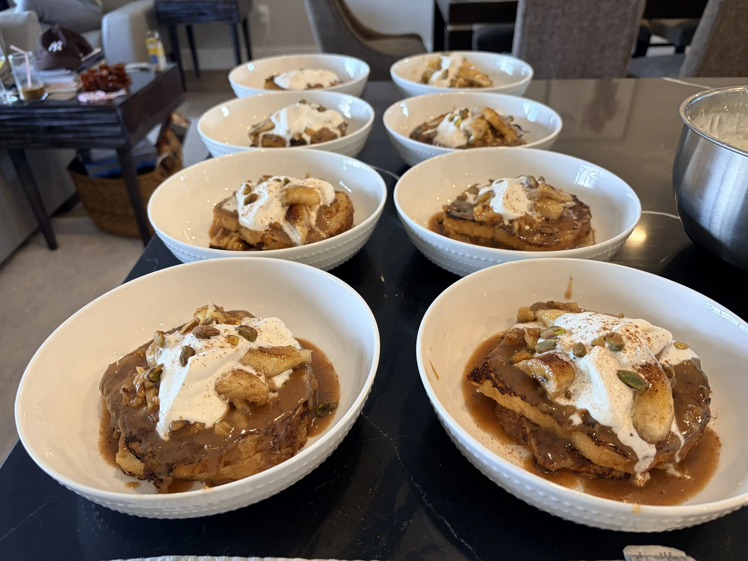 Multiple bowls of French toast topped with whipped cream, caramelized bananas and fosters sauce.