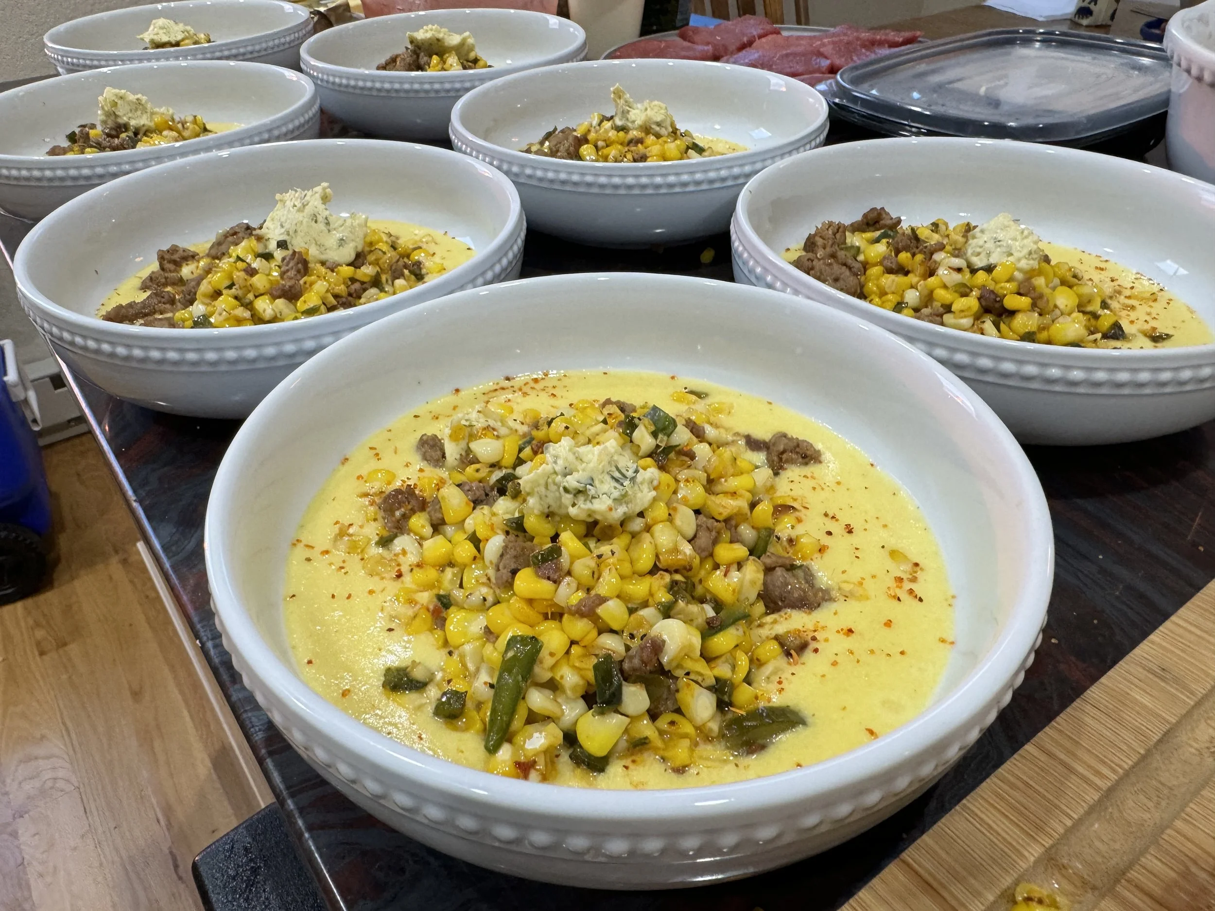 Bowl of creamed corn topped with Chorizo, corn kernels, diced green peppers, and a dollop of salsa Verde butter, sprinkled with tajin