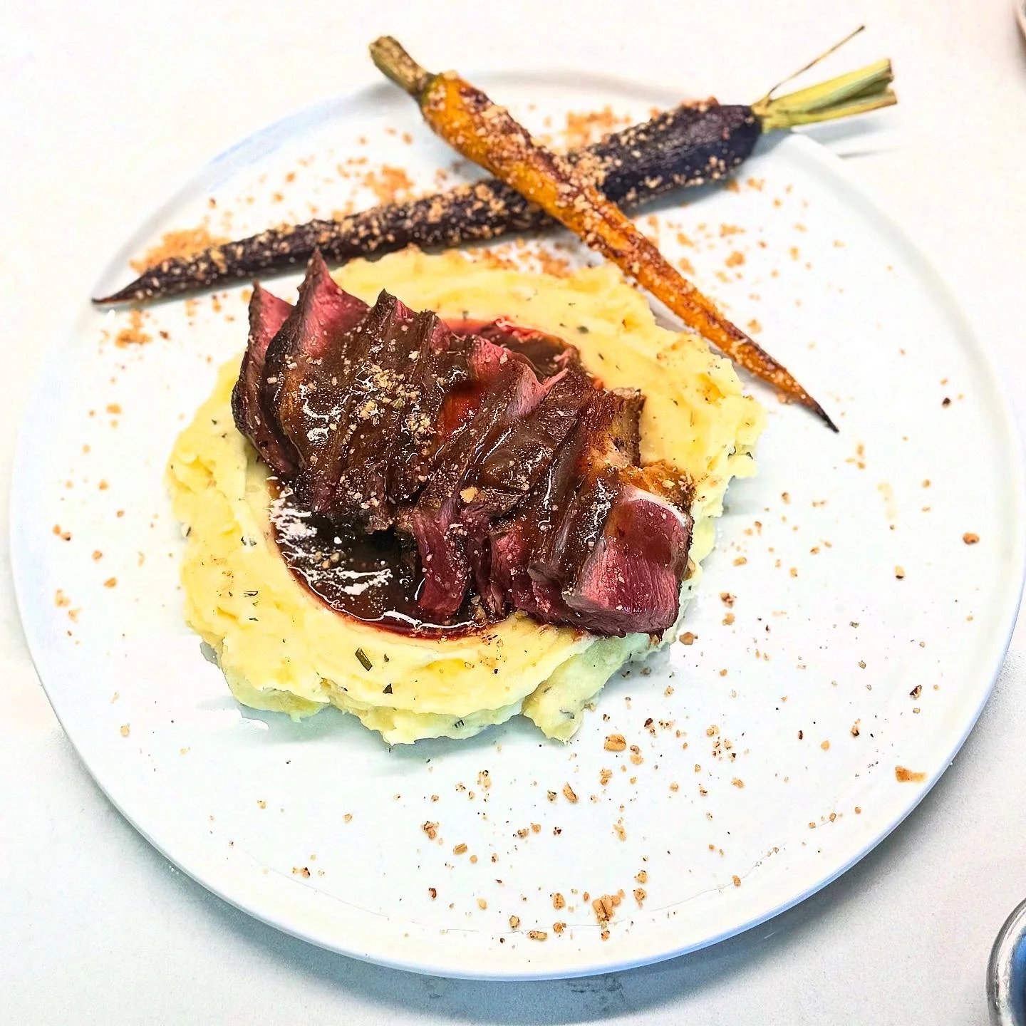 Plate of mashed potatoes with beef steak and grilled carrots garnished with spices.