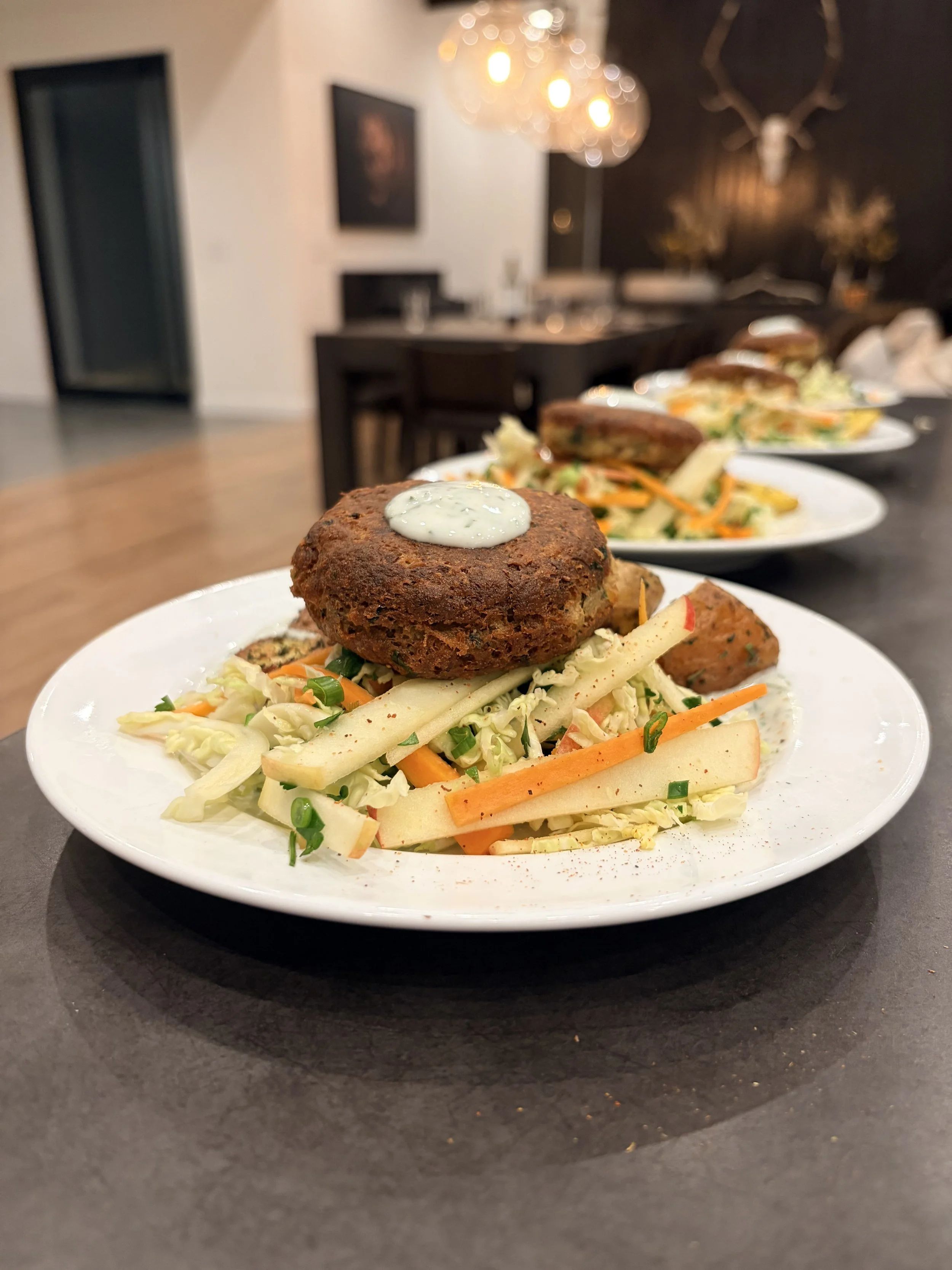 Plate of crabcakes with a dollop of white sauce on top, served with salad and apple slices on a white plate in a restaurant setting.