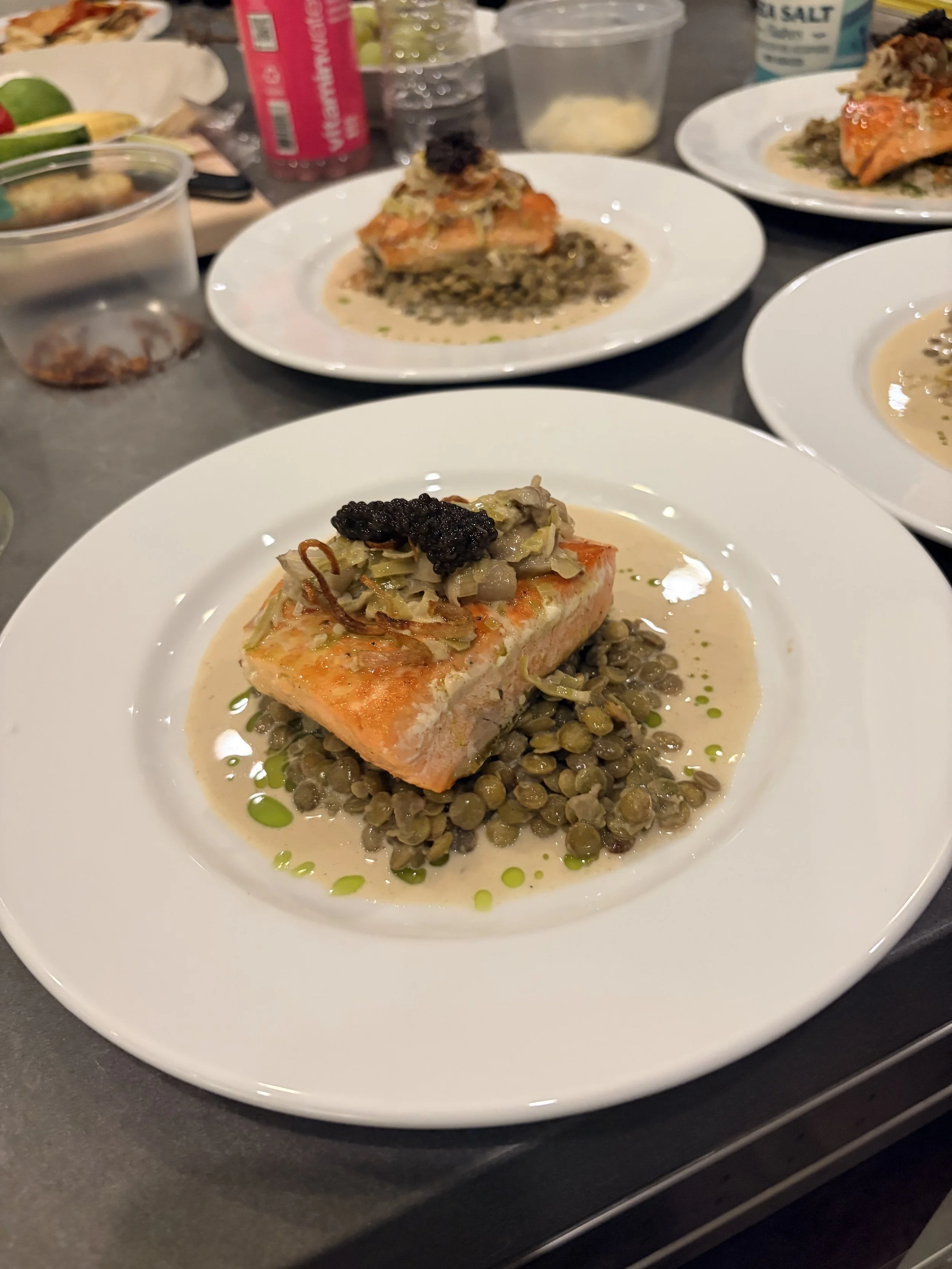 A plated dish of cooked salmon topped with a relish on a bed of lentils, garnished with a dollop of black caviar, on a white plate.