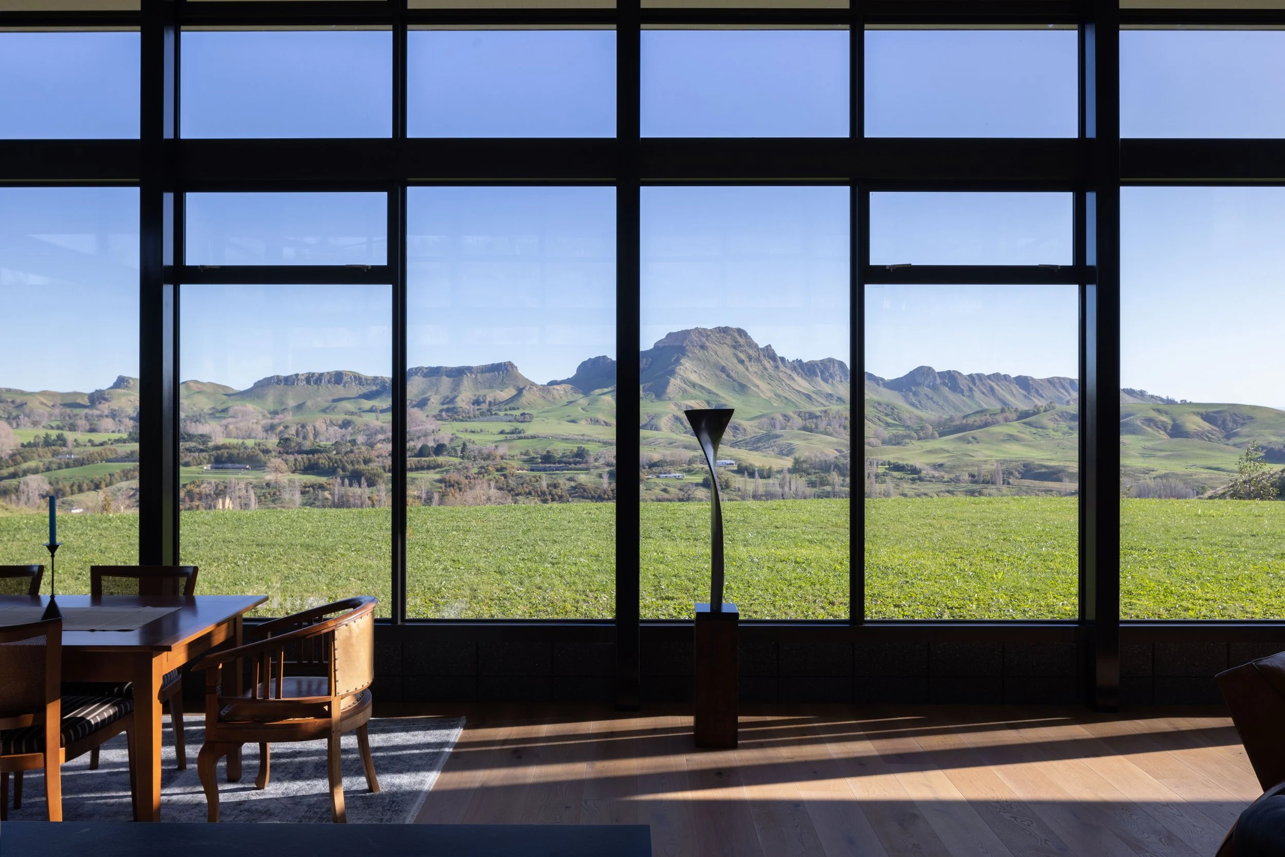 Interior of a room with large floor-to-ceiling windows showing a scenic landscape of green hills and mountains under a clear blue sky.
