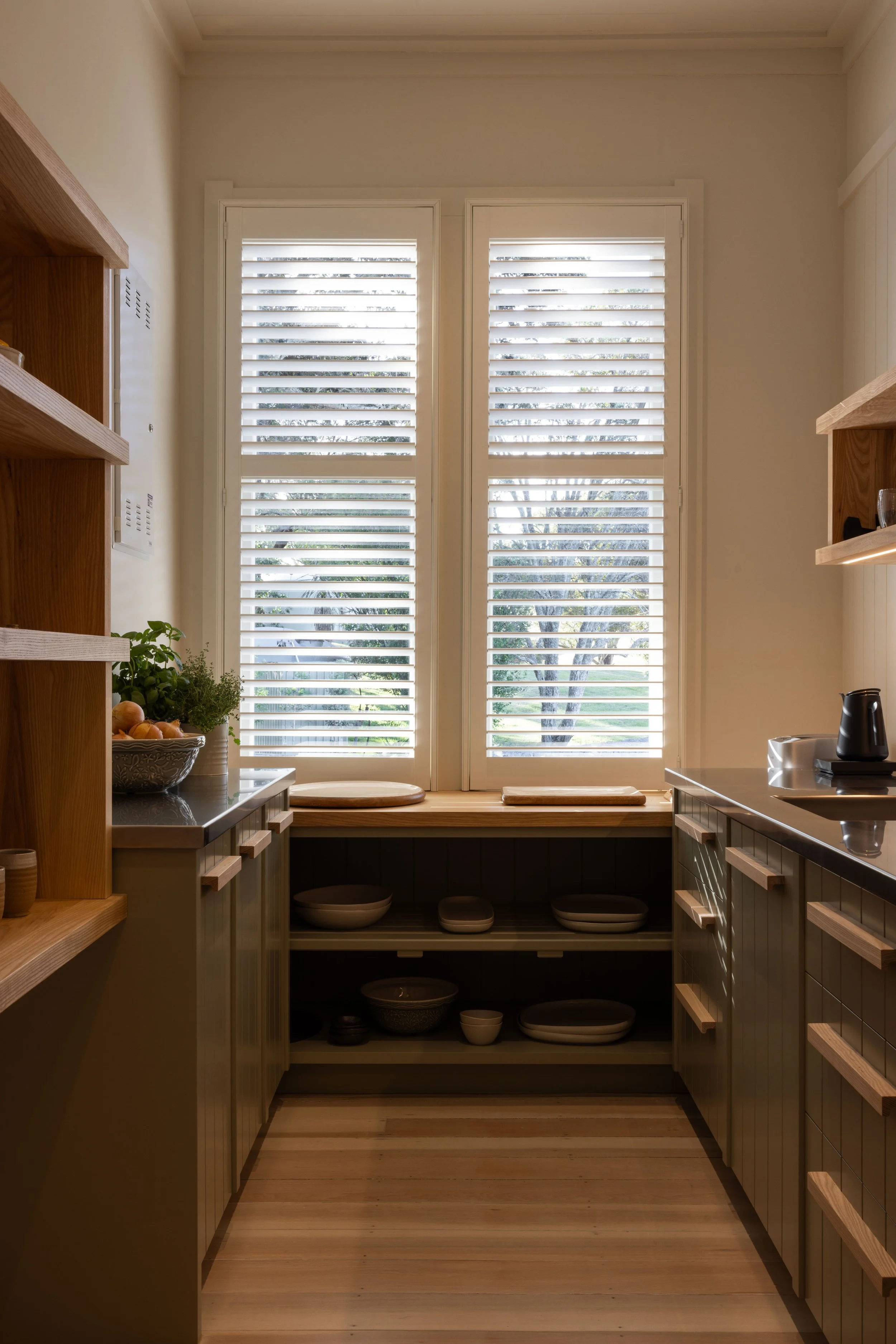 A cozy kitchen with wooden shelves, white shutters and timber flooring by Terrain Timber Flooring Hawke's Bay.