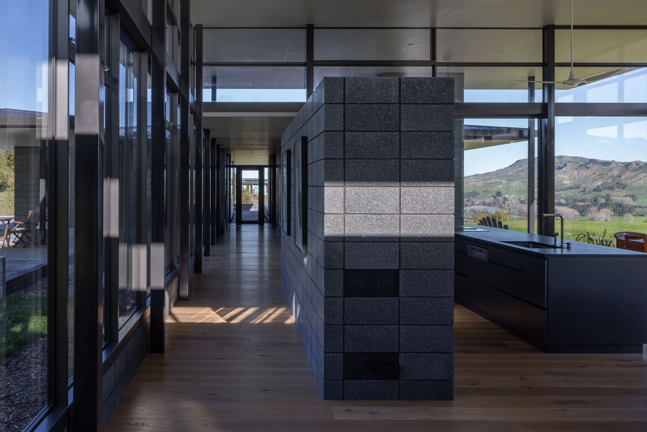 Modern interior space with glass walls, wooden flooring, and a view of green hills outside.