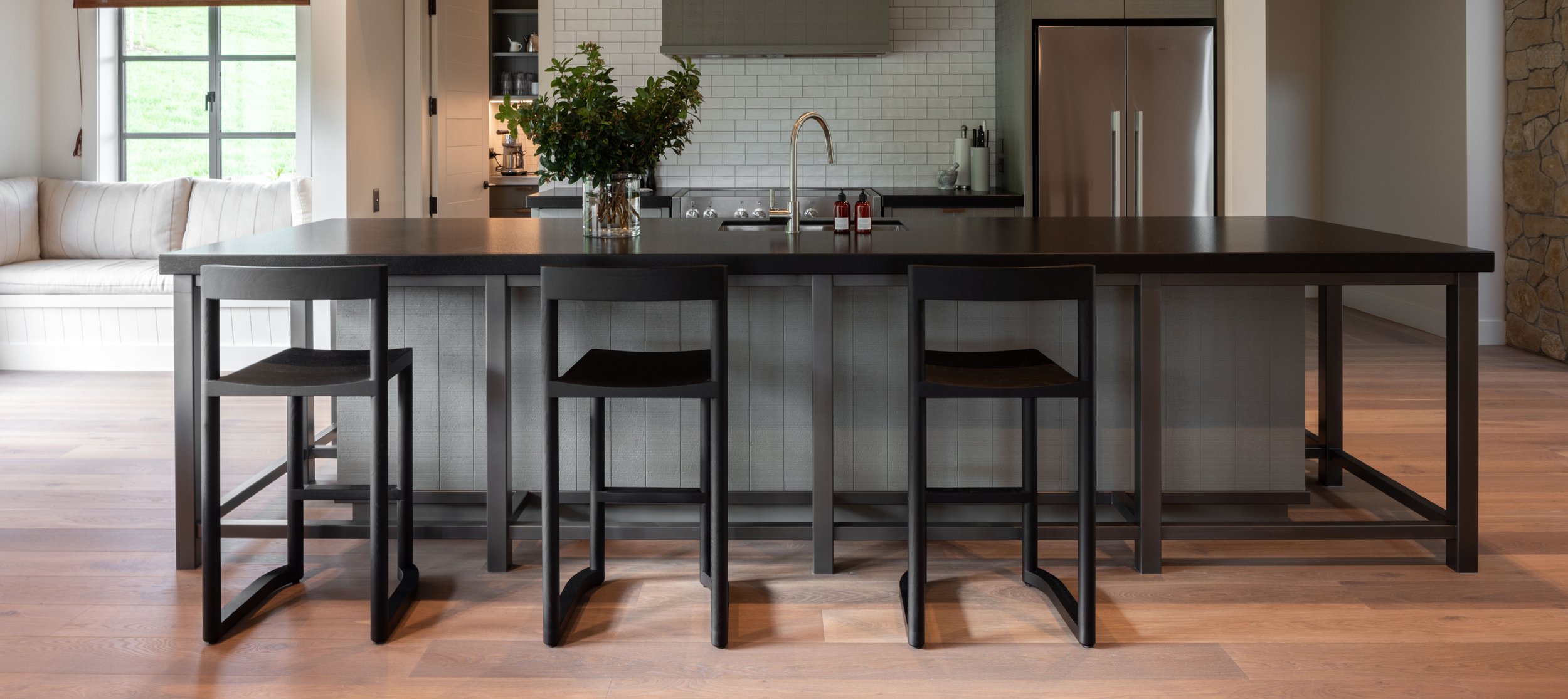 A modern kitchen with a large black island and three black stools and engineered timber flooring by Terrain.