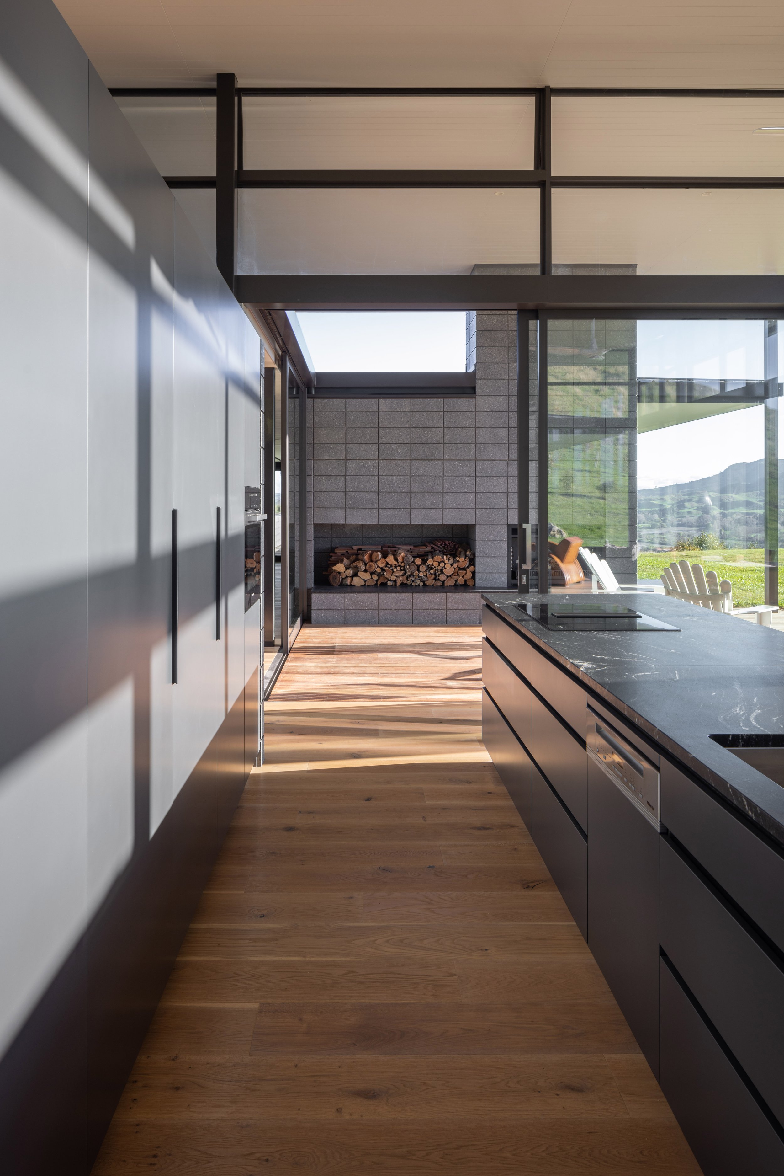 Modern kitchen with black cabinetry, wooden flooring, and large windows overlooking a mountain landscape.