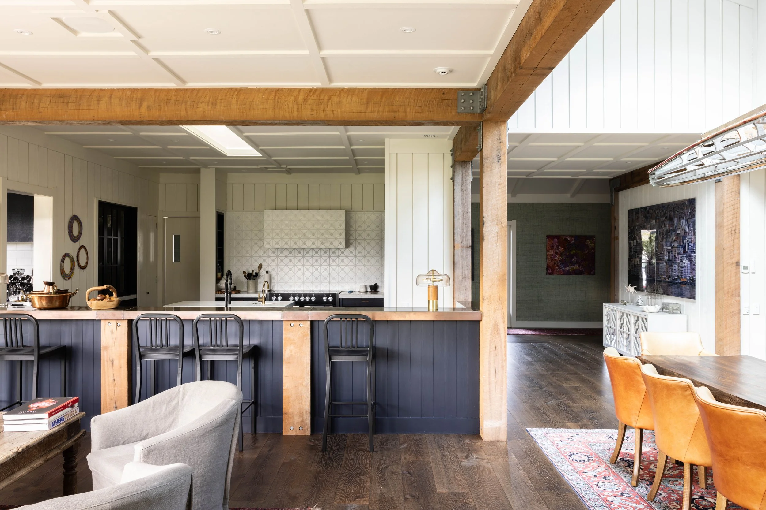 Open-concept kitchen and dining area with wooden beams, white shiplap walls, dark wood flooring, and modern furniture