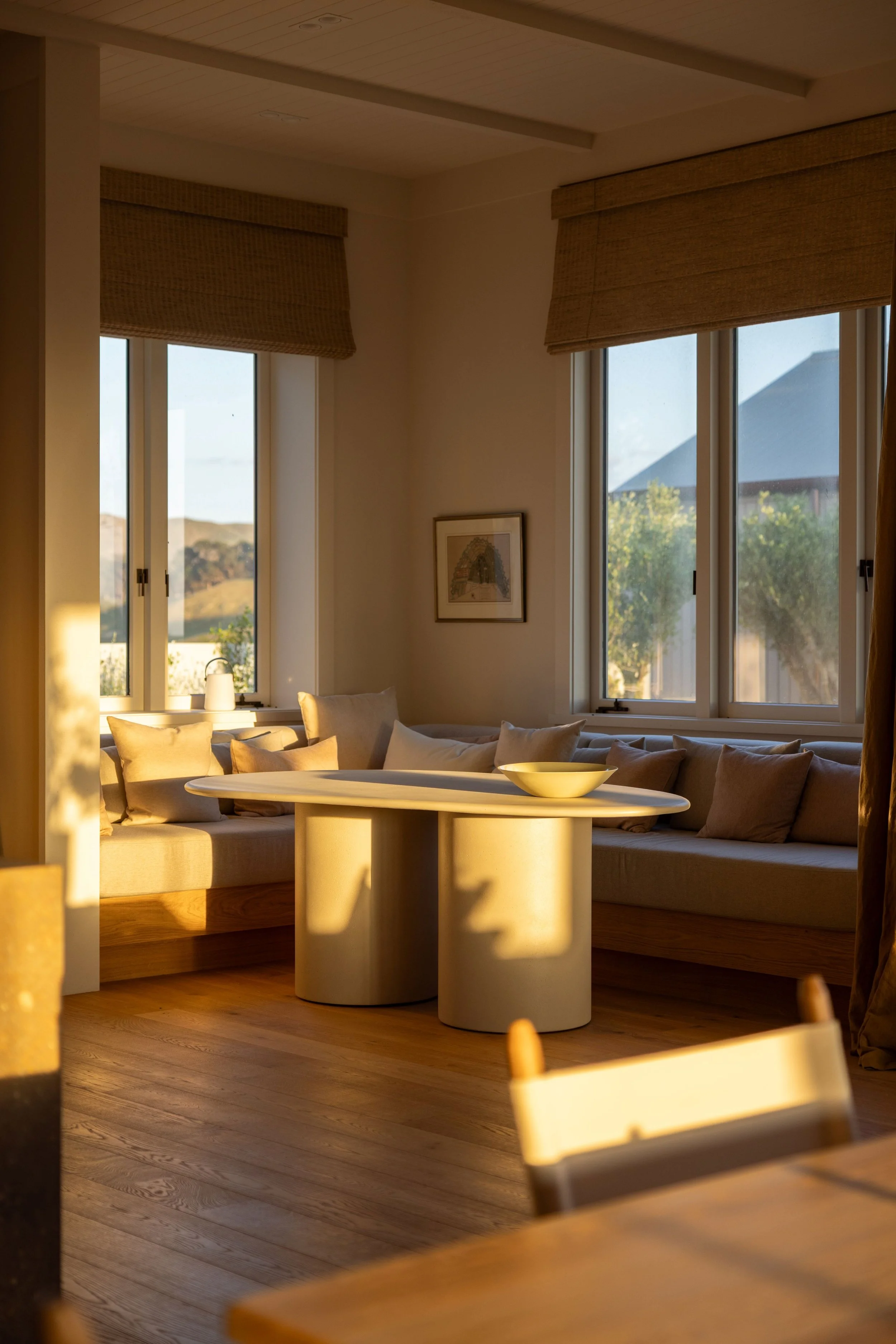 A cozy living room with sunlight streaming through large windows onto timber flooring by Terrain, Hawke's Bay.