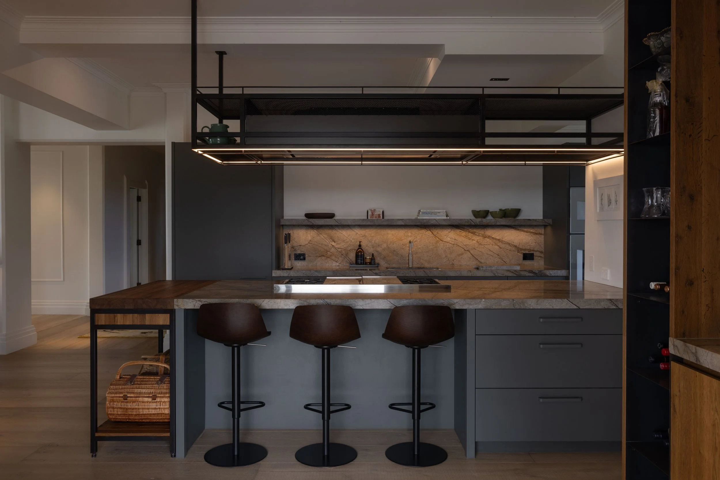 Modern kitchen with gray cabinetry, marble backsplash, wooden countertops, and three black barstools.