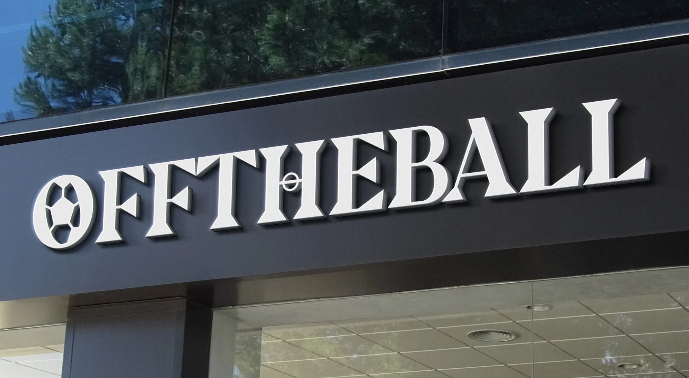 Sign for Off The Wall with a sports ball logo featuring a soccer ball, mounted on a dark exterior wall of a building, with reflective glass windows above.