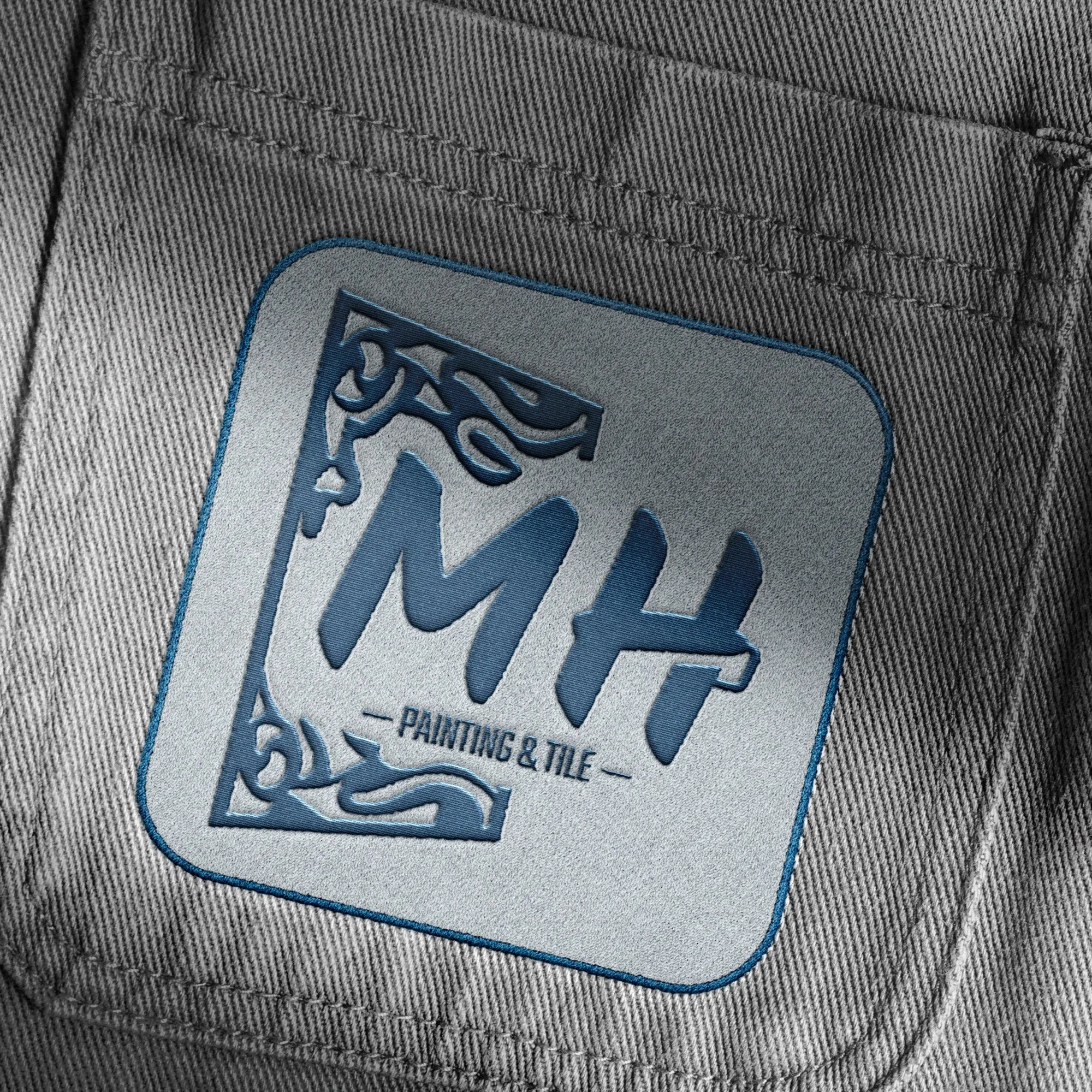 Close-up of a dark grey fabric label with the text 'MH Painting & Tile' in blue and black outlining, stitched onto a grey textured fabric.