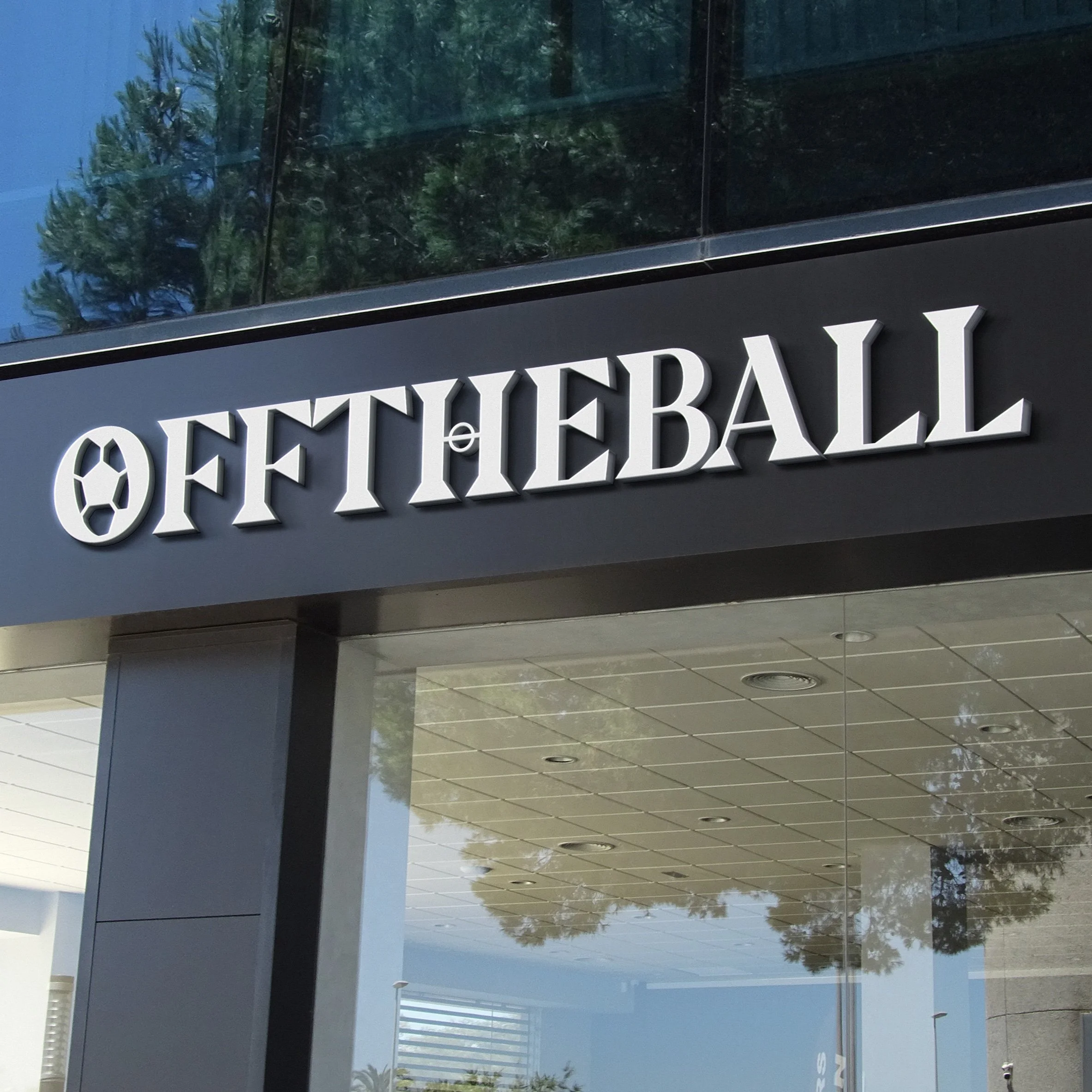 Sign for Off The Wall with a sports ball logo featuring a soccer ball, mounted on a dark exterior wall of a building, with reflective glass windows above.