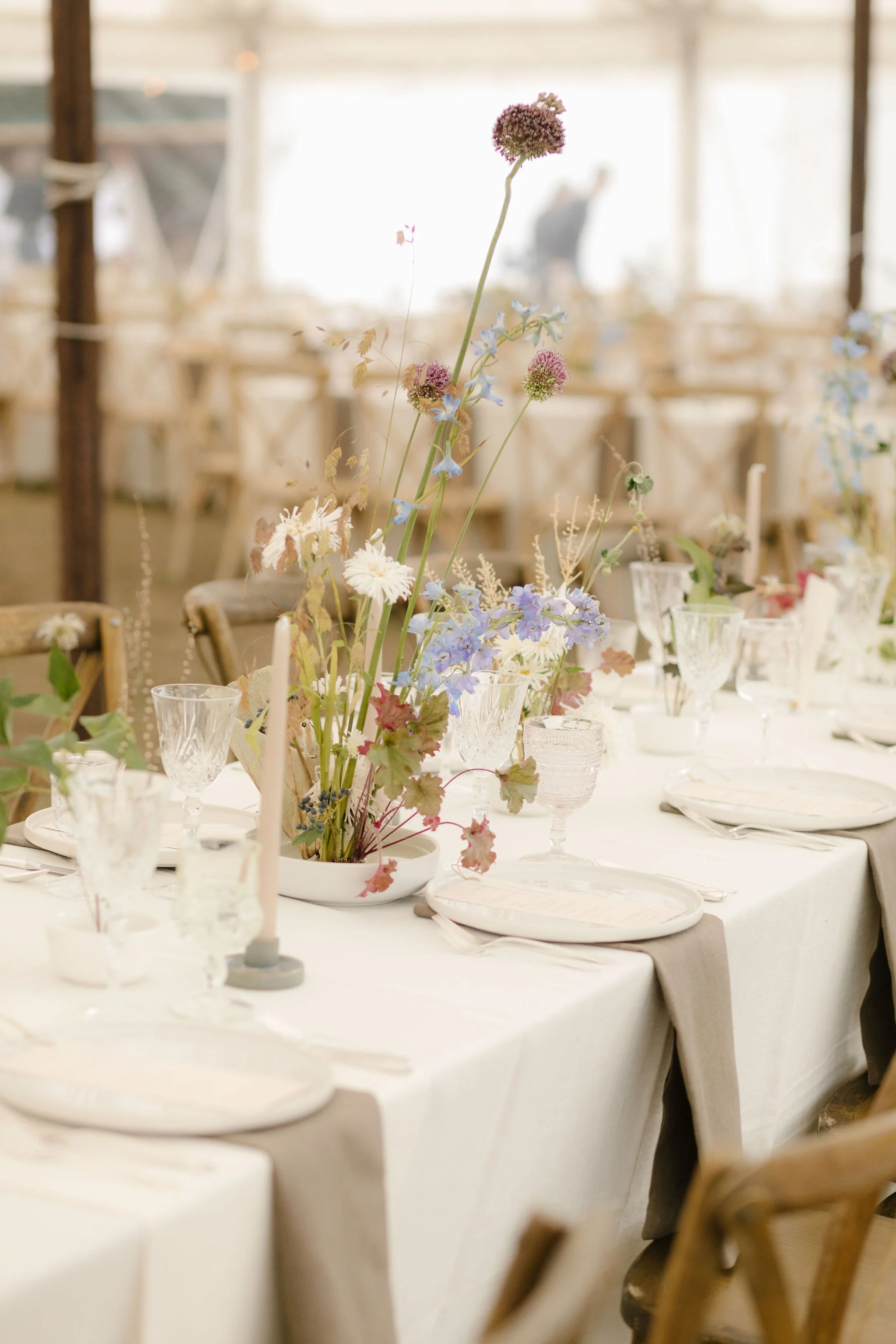 Elegant dining table with a floral centerpiece, set with glasses, plates, and candles, in a bright room with natural light.
