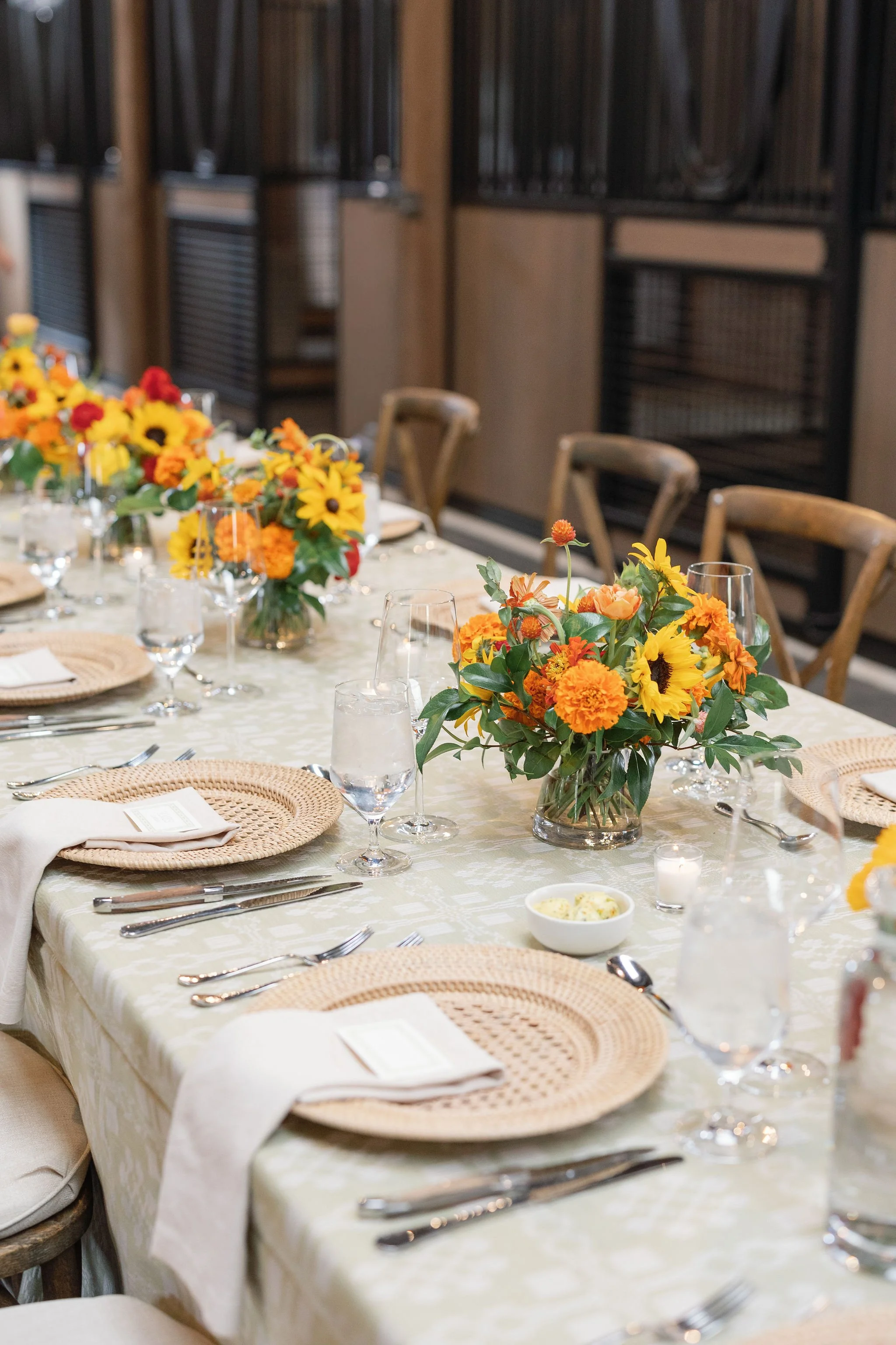Close detail of wedding reception table with sunflower and warm-toned floral centerpiece, gold charger plates, and linen napkins, by Wild Blume