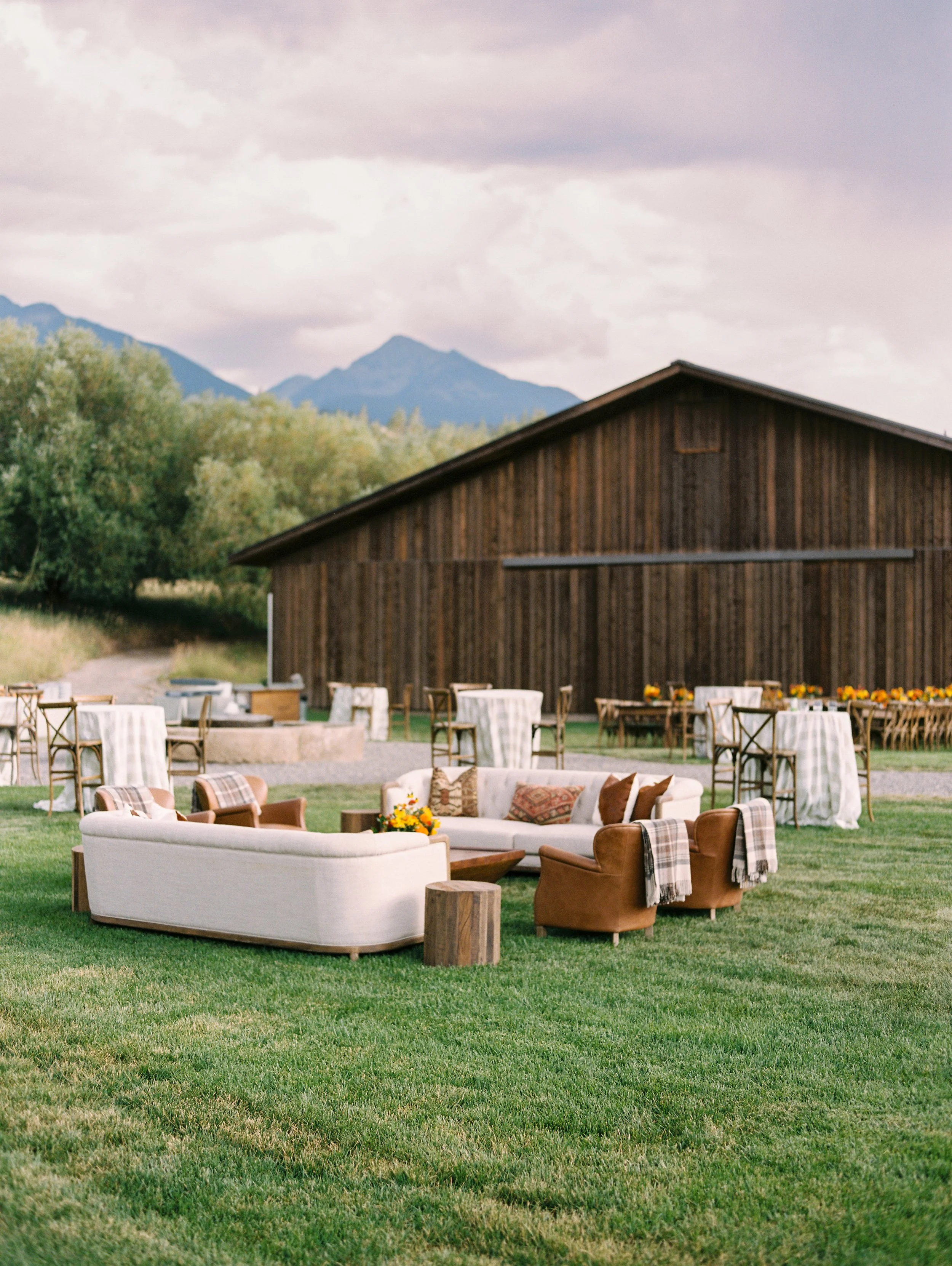 Outdoor wedding reception with long white tables and floral centerpieces set beside a rustic Montana barn, designed by Wild Blume