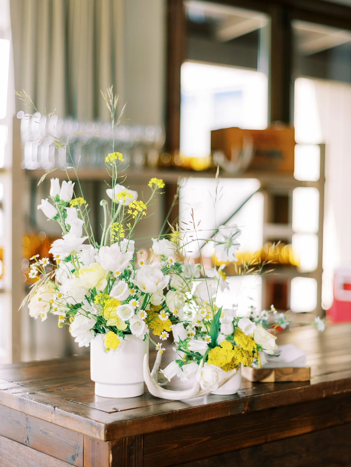 A bouquet of white and yellow flowers on a wooden table in a bright interior space