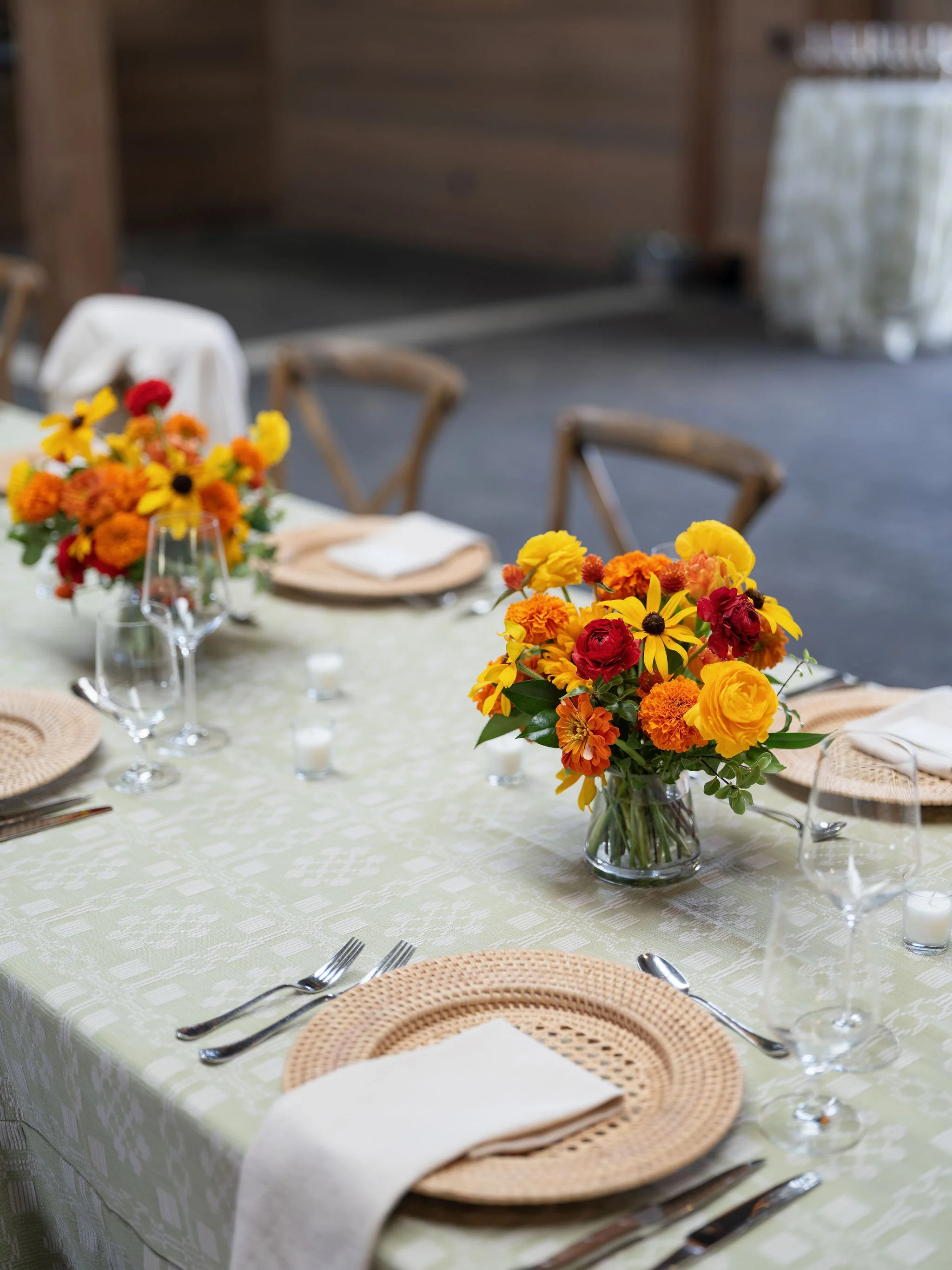 Close detail of wedding reception table with sunflower and orange bloom centerpiece, linen napkins, and warm place settings, by Wild Blume