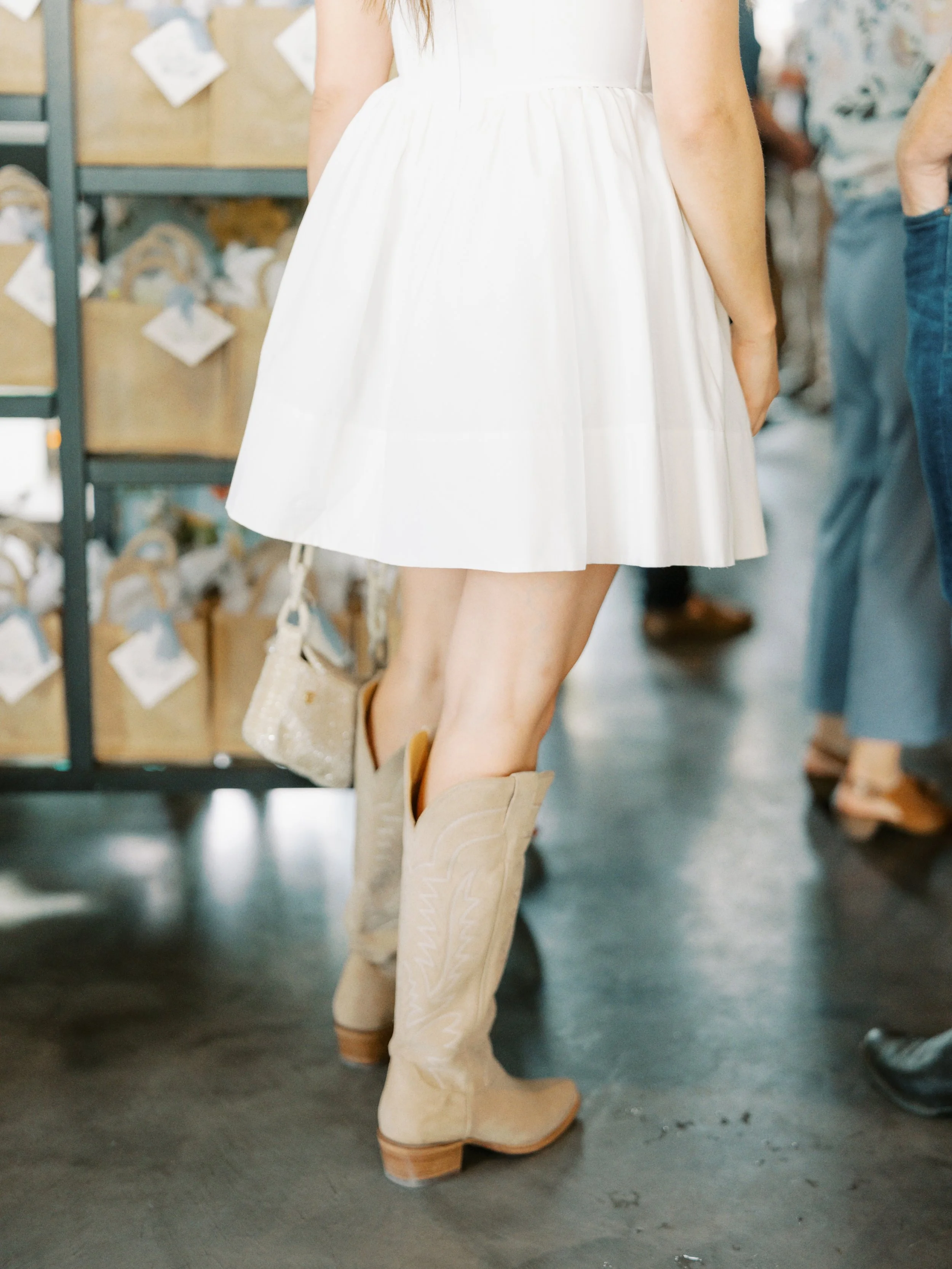 Person wearing a white dress and tan cowboy boots at a store, with shelves in the background.