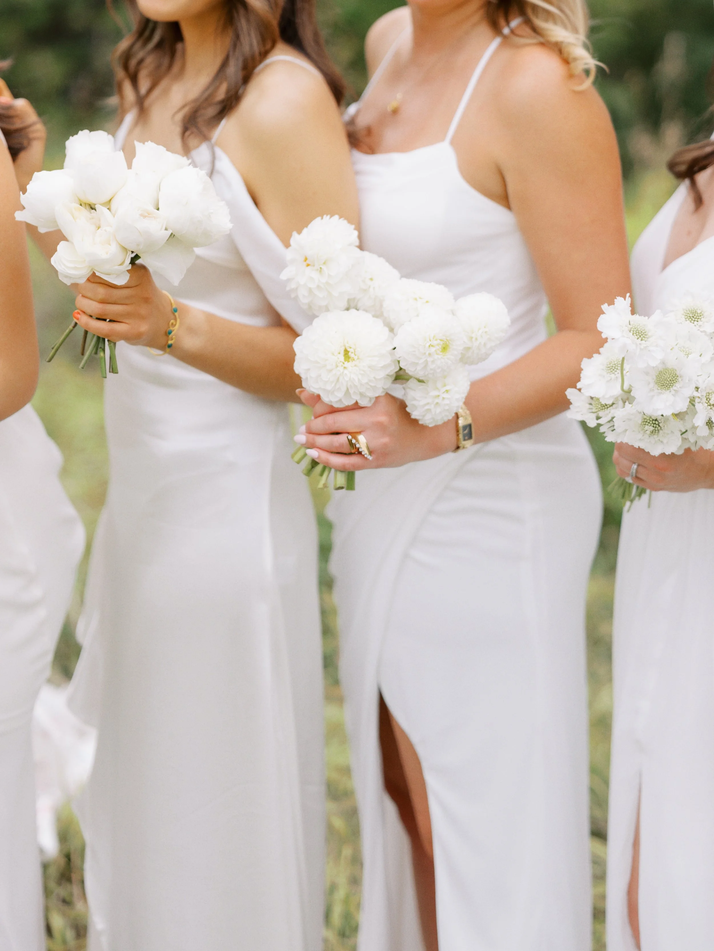 Women in white dresses holding white flower bouquets during an outdoor event.