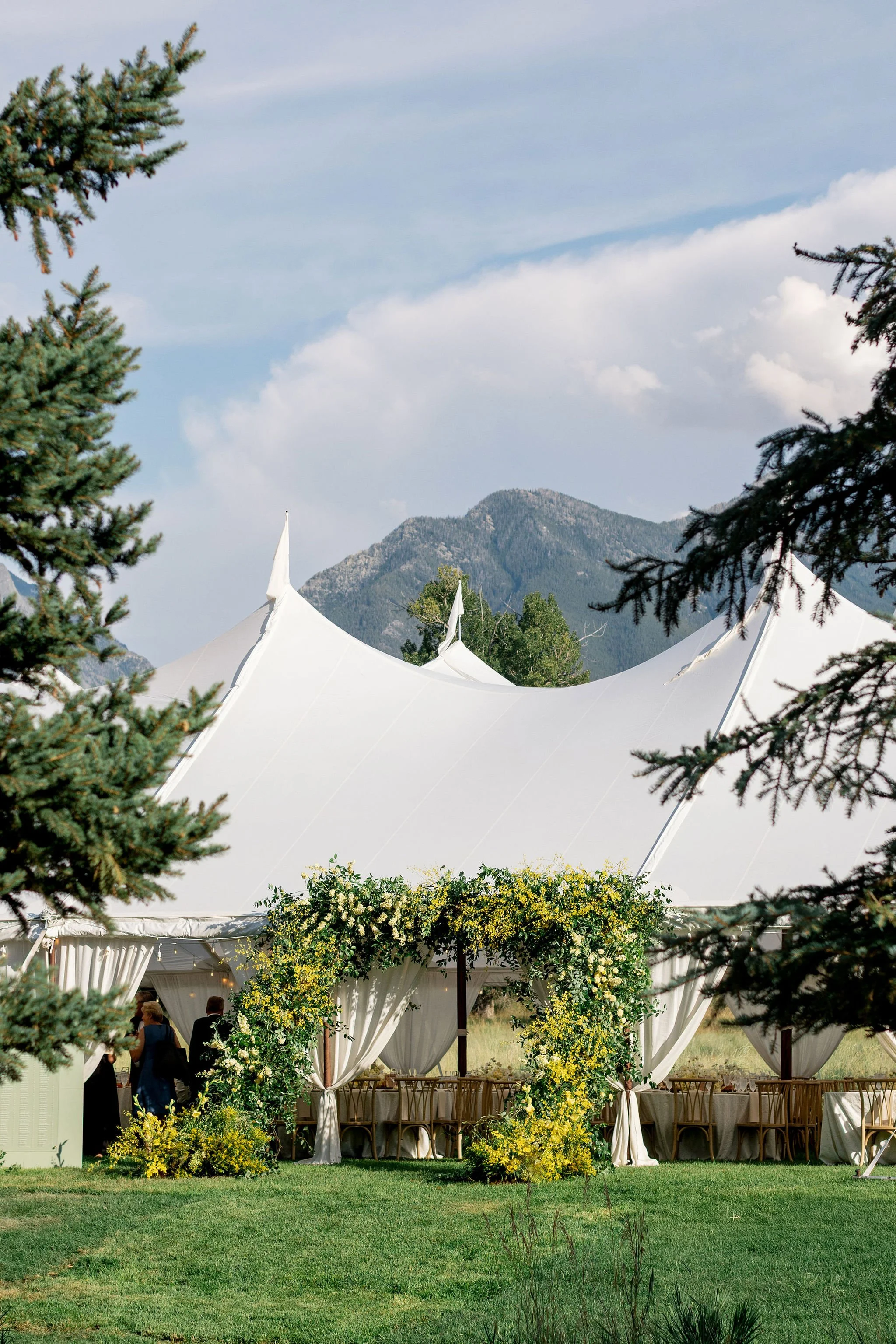 White sailcloth wedding tent set against a Montana mountain landscape with tall pine trees and soft cloudy sky