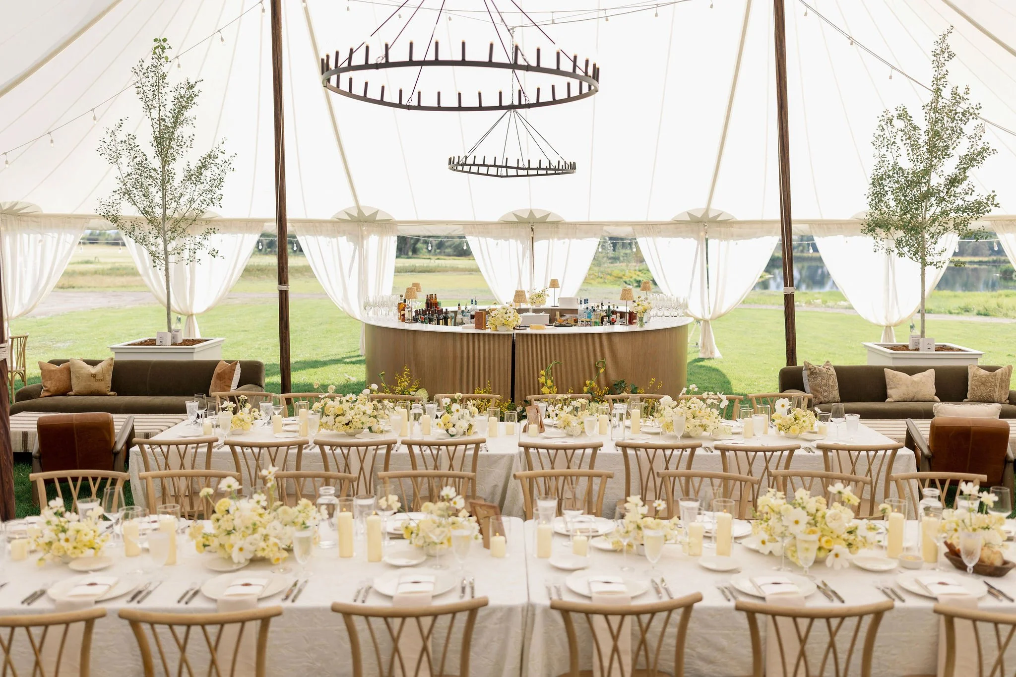 Elegant tented wedding reception interior with draped curtains, central bar with florals, long dining tables, and warm lighting, designed by Wild Blume