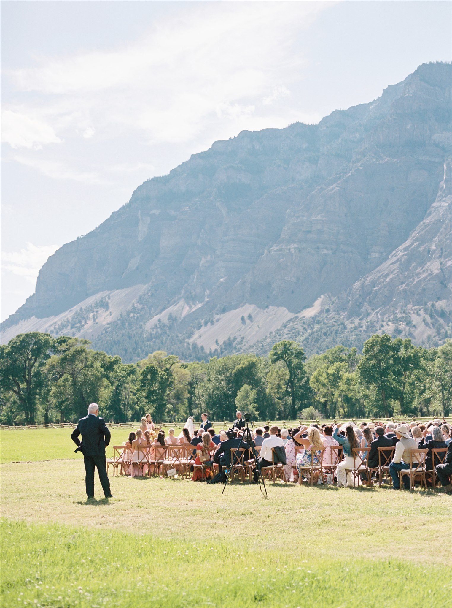 Outdoor wedding ceremony with guests seated in a green field beneath a dramatic Montana mountain backdrop, designed by Wild Blume
