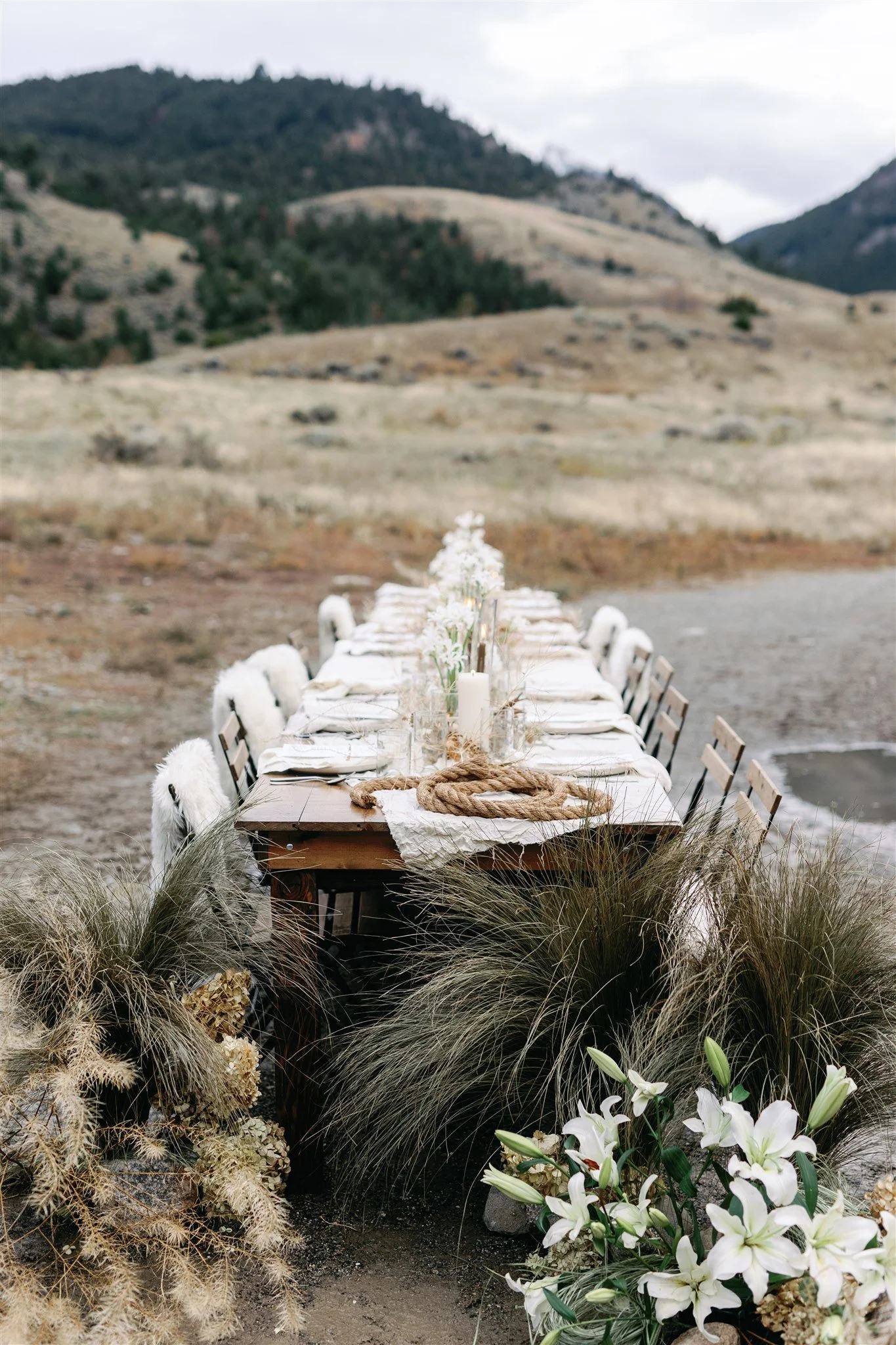 Intimate outdoor dining table styled with white florals and pampas grass set against a wide open Montana prairie landscape, by Wild Blume