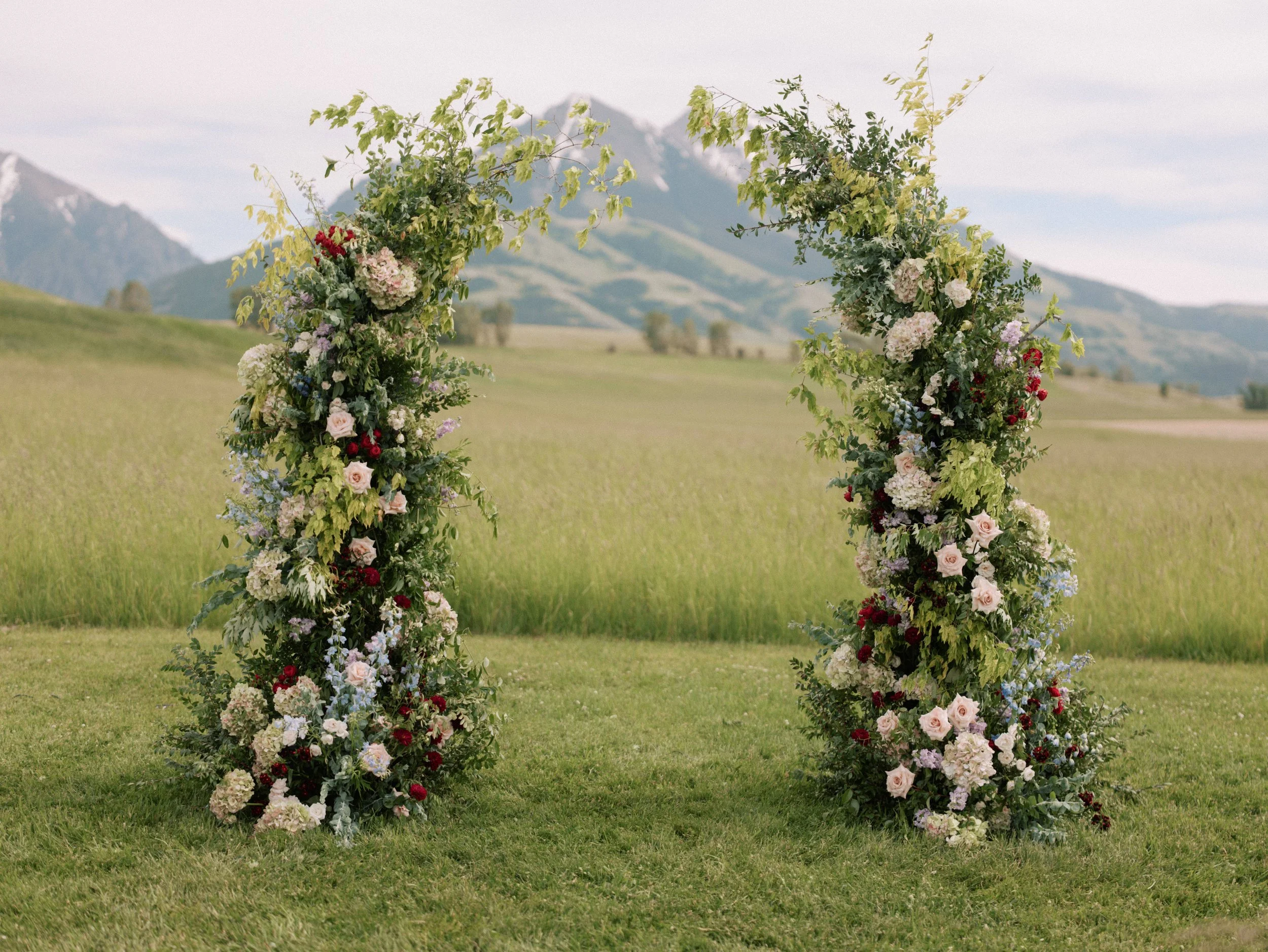 Green and white floral ceremony arch in an open Montana field, designed by Wild Blume