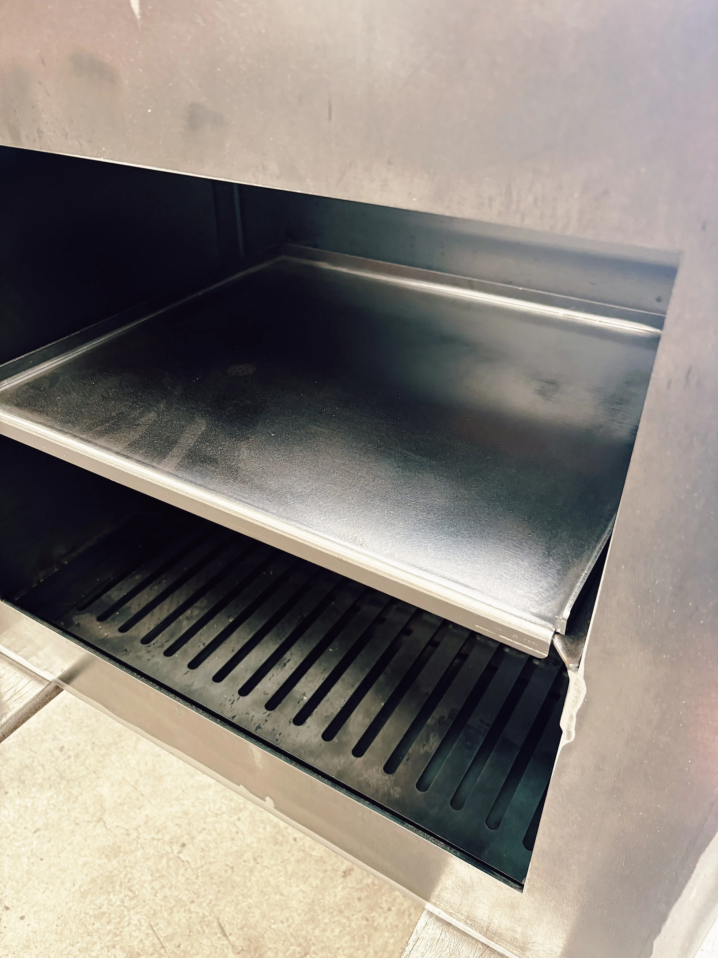 Empty stainless steel snack or oven drawer with a vented tray and a shelf above.