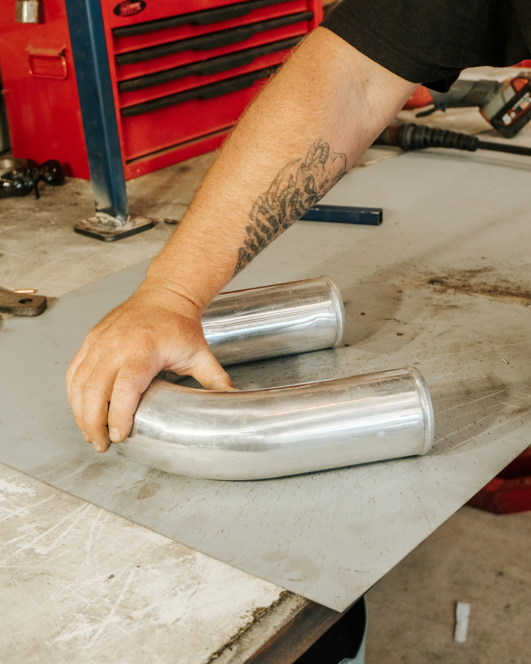 A person is working with two curved metal pipes on a workbench in a workshop.