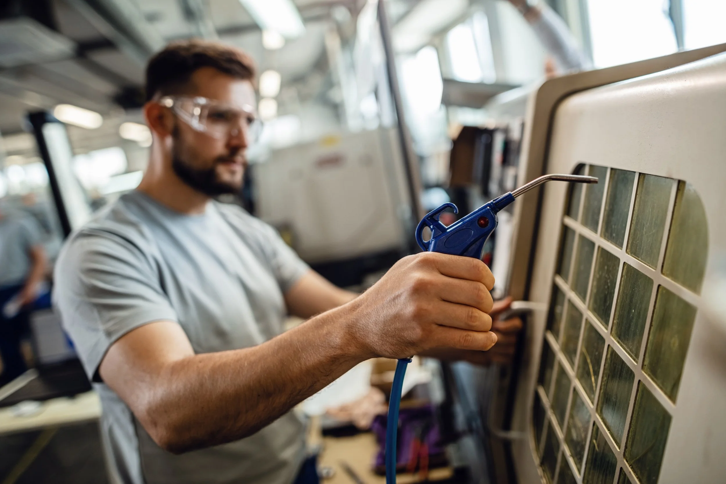 Un homme portant des lunettes de protection utilise une panne à souder sur une matrice de composants électroniques, dans un atelier de réparation ou de fabrication.