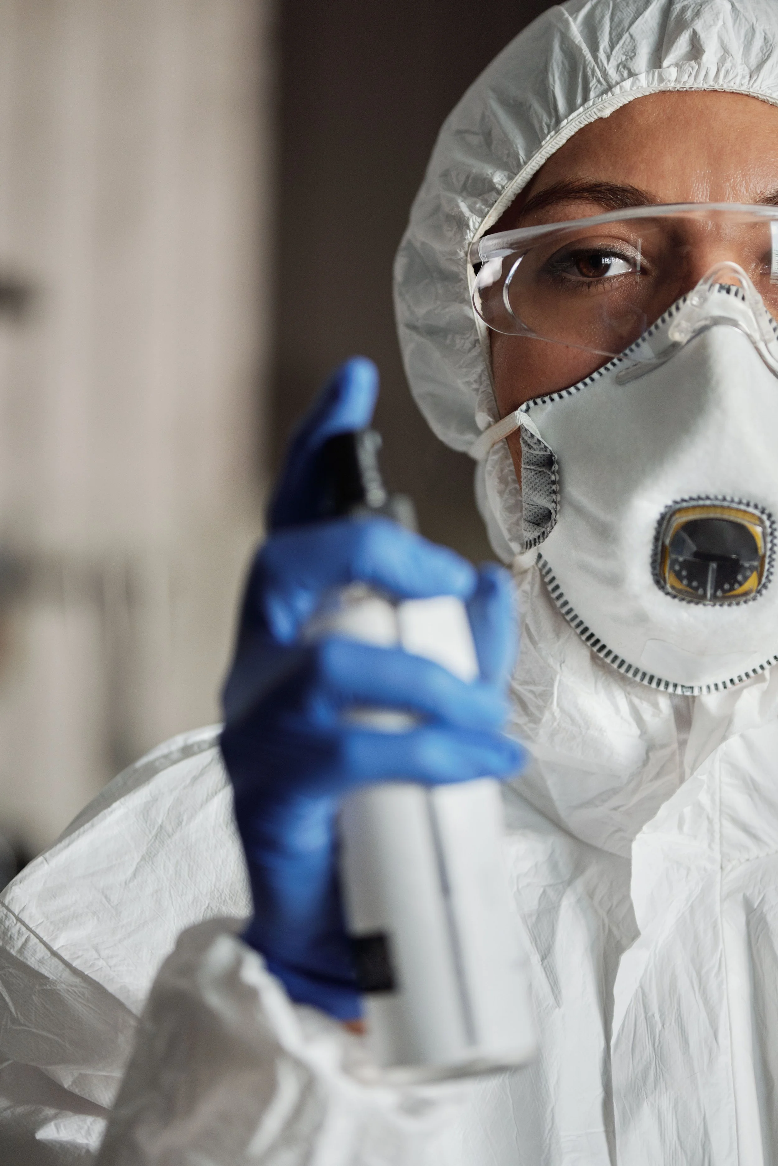 Un professionnel en équipement de protection individuelle, y compris un masque, des lunettes de protection, une combinaison blanche et des gants bleus, manipulant un instrument médical ou de laboratoire.
