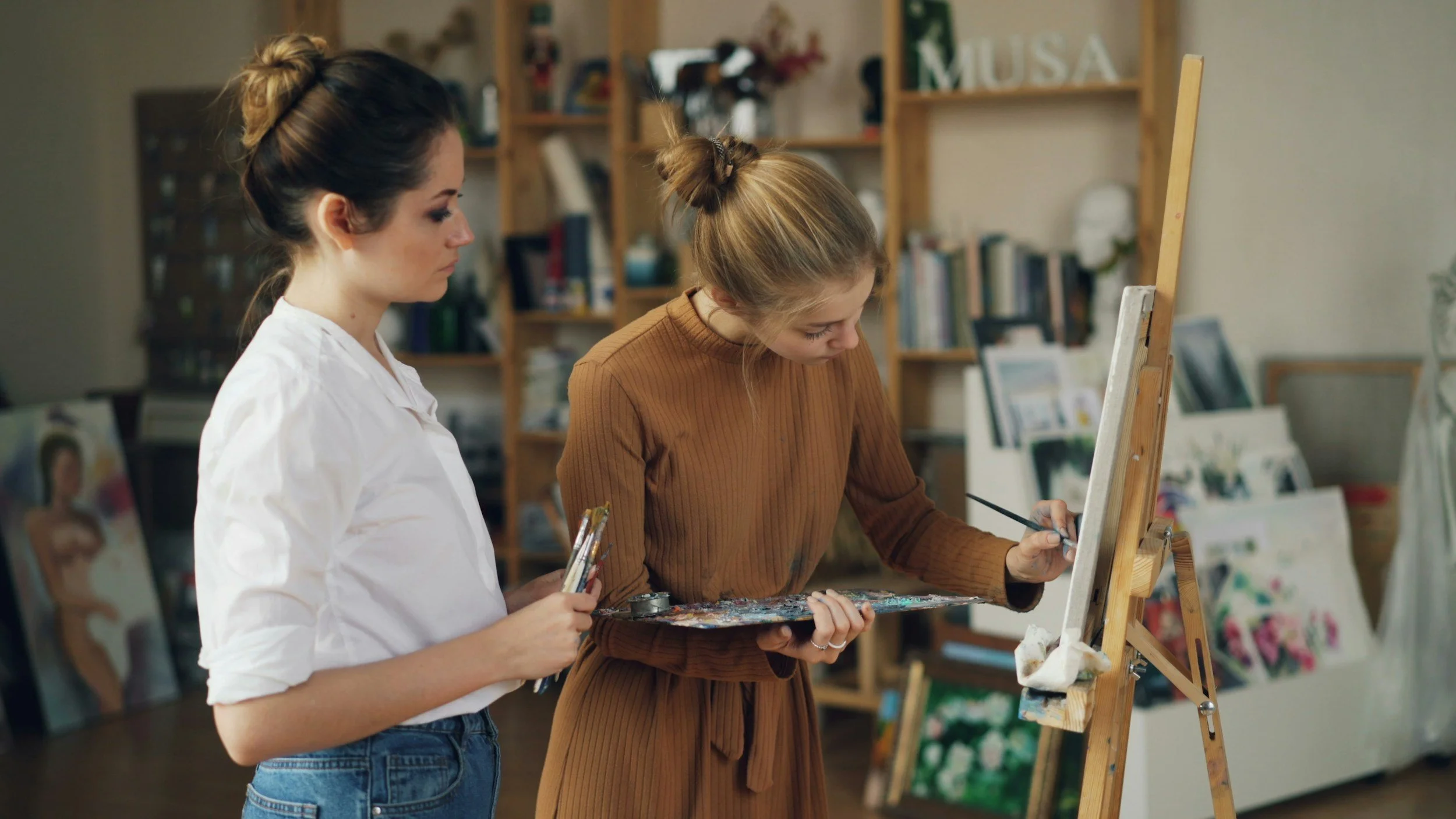 Two women painting on a canvas in an art studio.