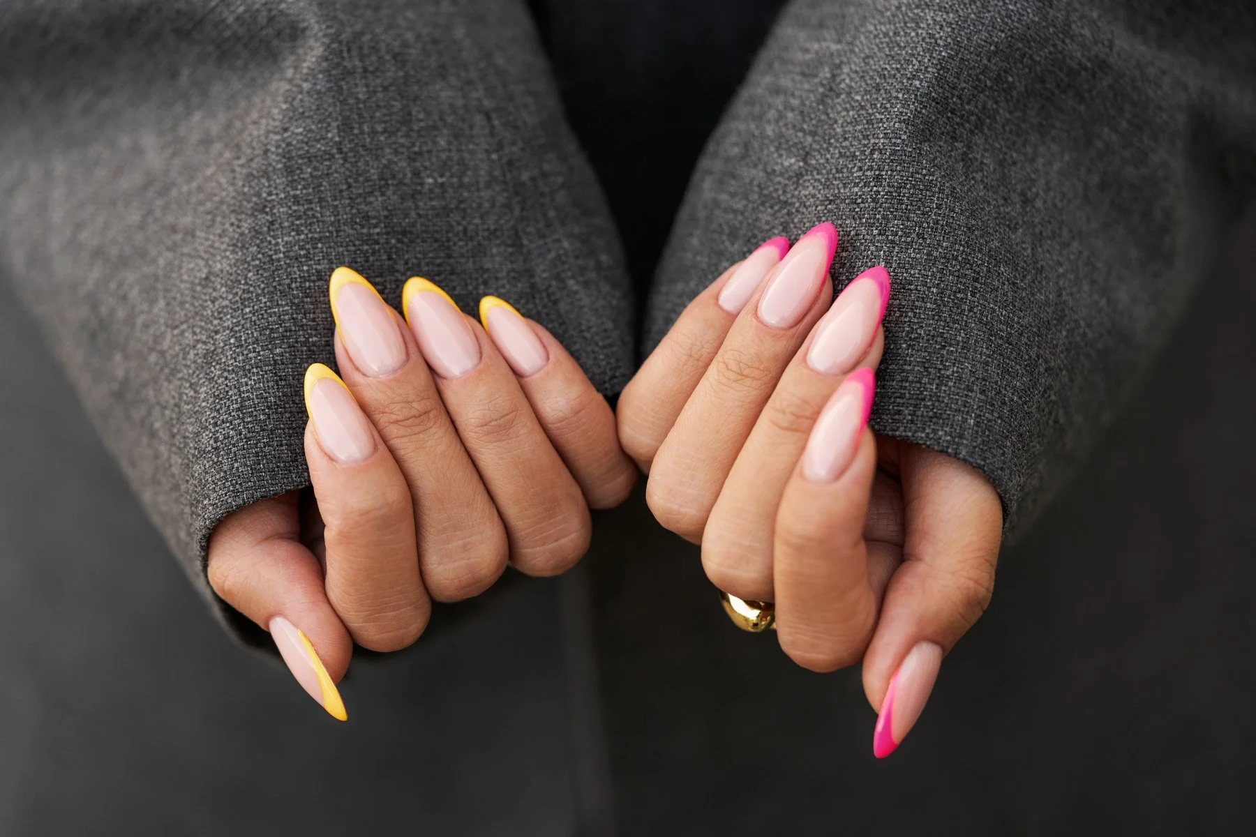 Close-up of hands with pink and yellow manicure, wearing a dark gray textured sleeve of a garment