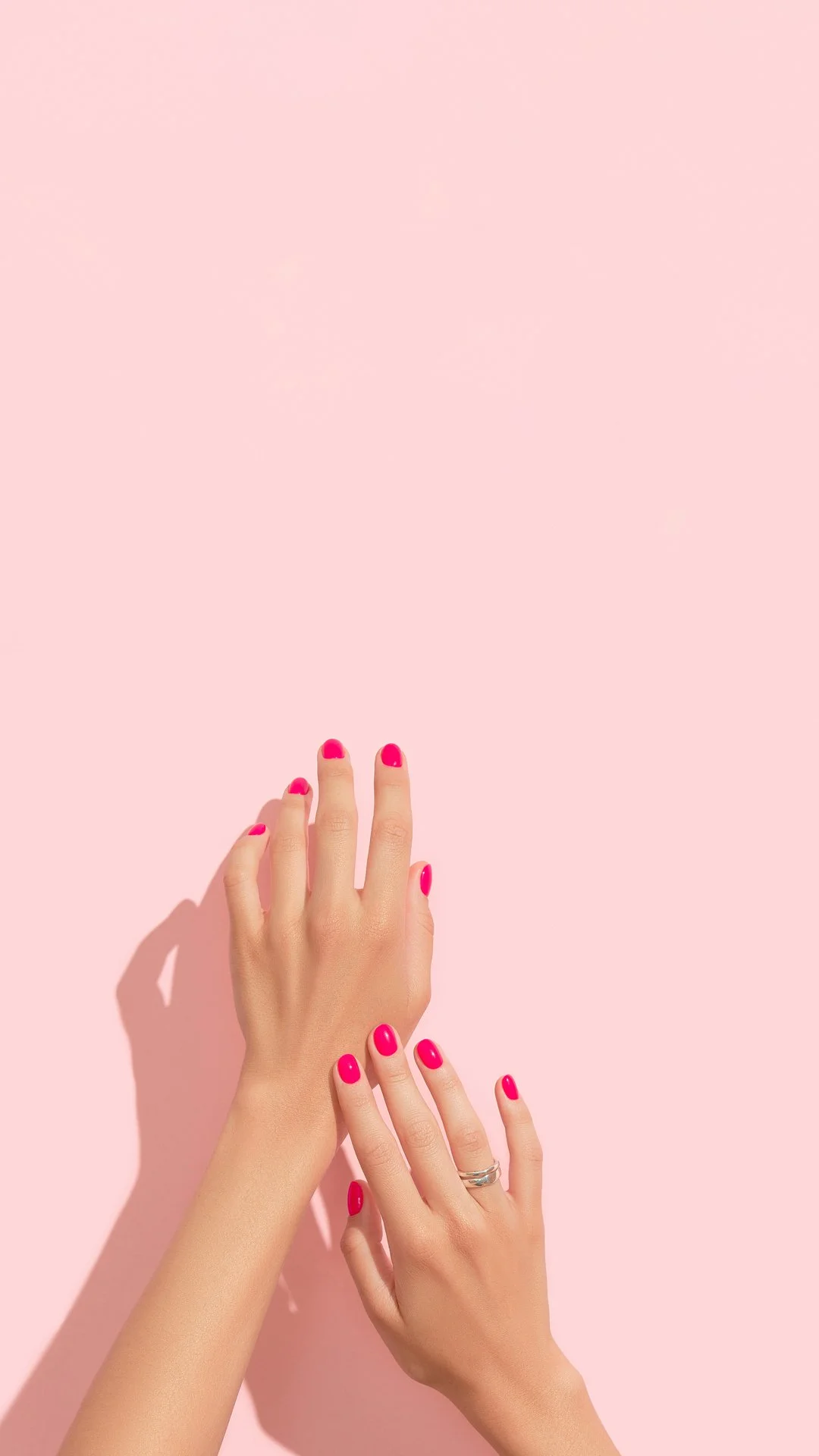 Two hands with pink nail polish touching against a pink background.