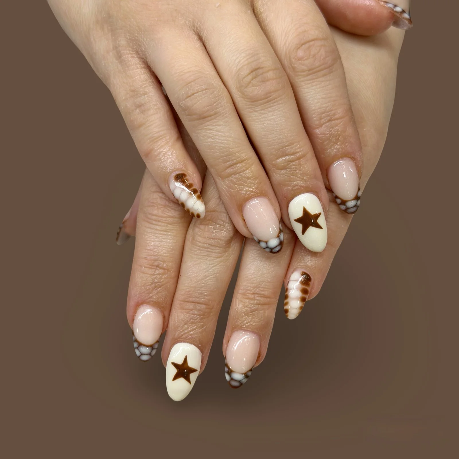 Close-up of hands with manicured nails featuring star and shell designs on a brown background.