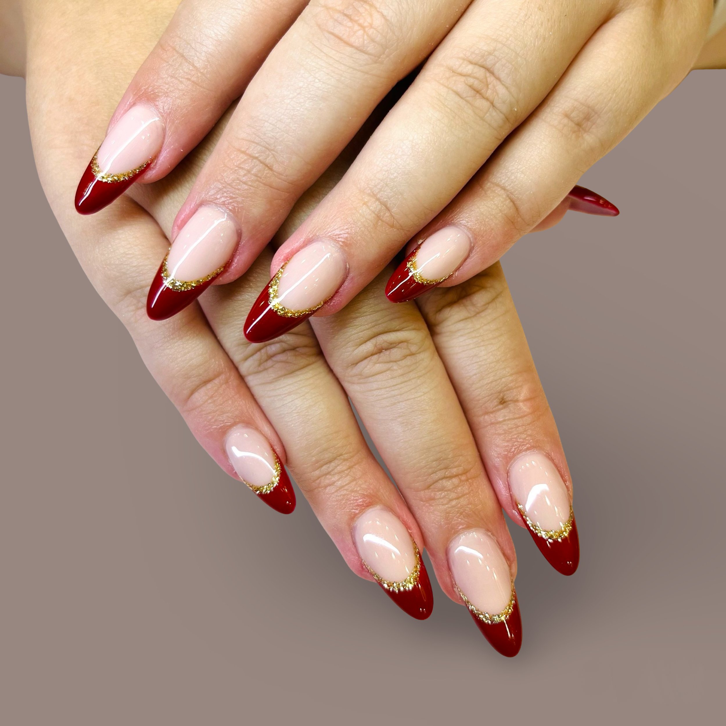 Close-up of hands with manicured nails featuring red tips, gold glitter accents, and nude base.