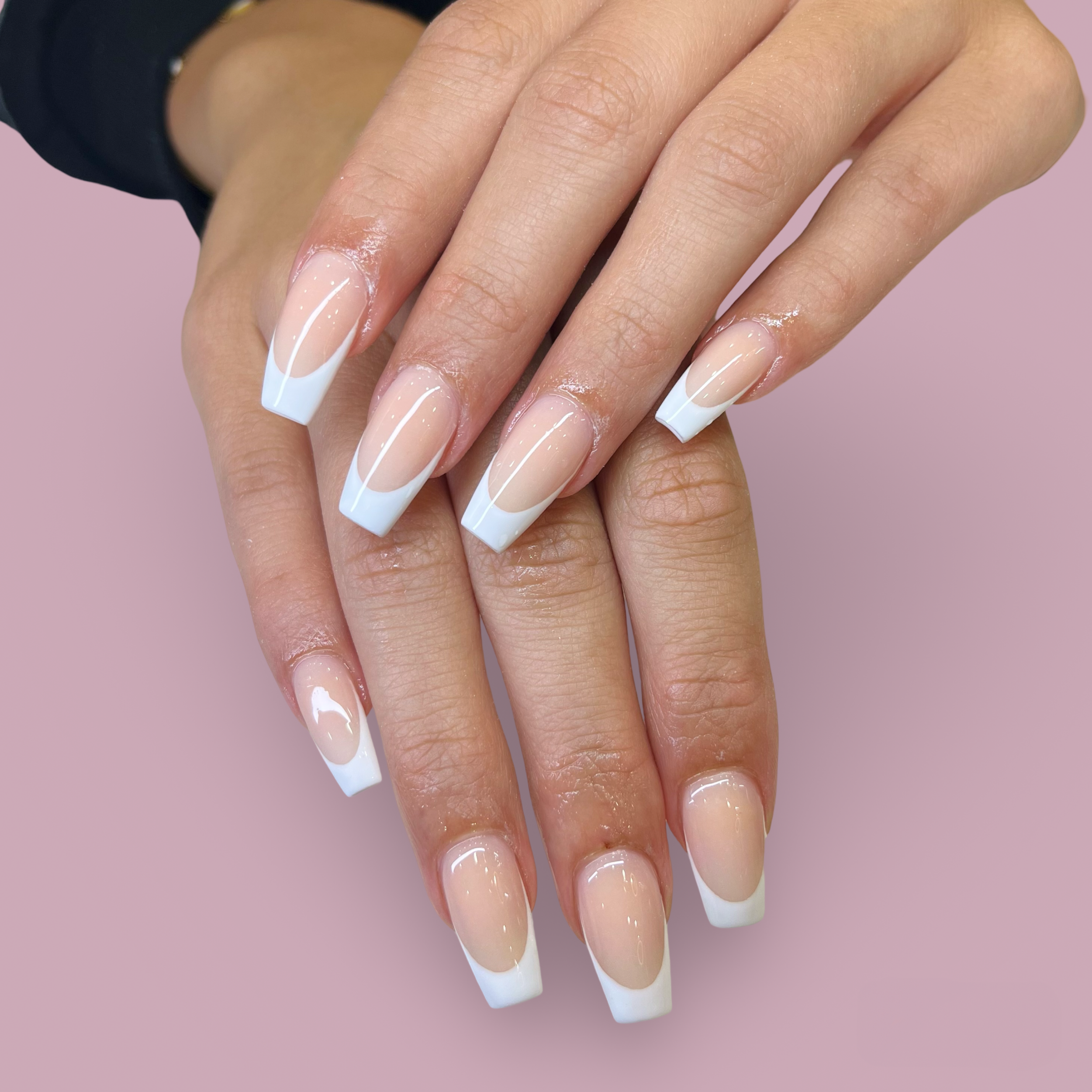 Hands with manicured nails featuring white French tips against a pink background.