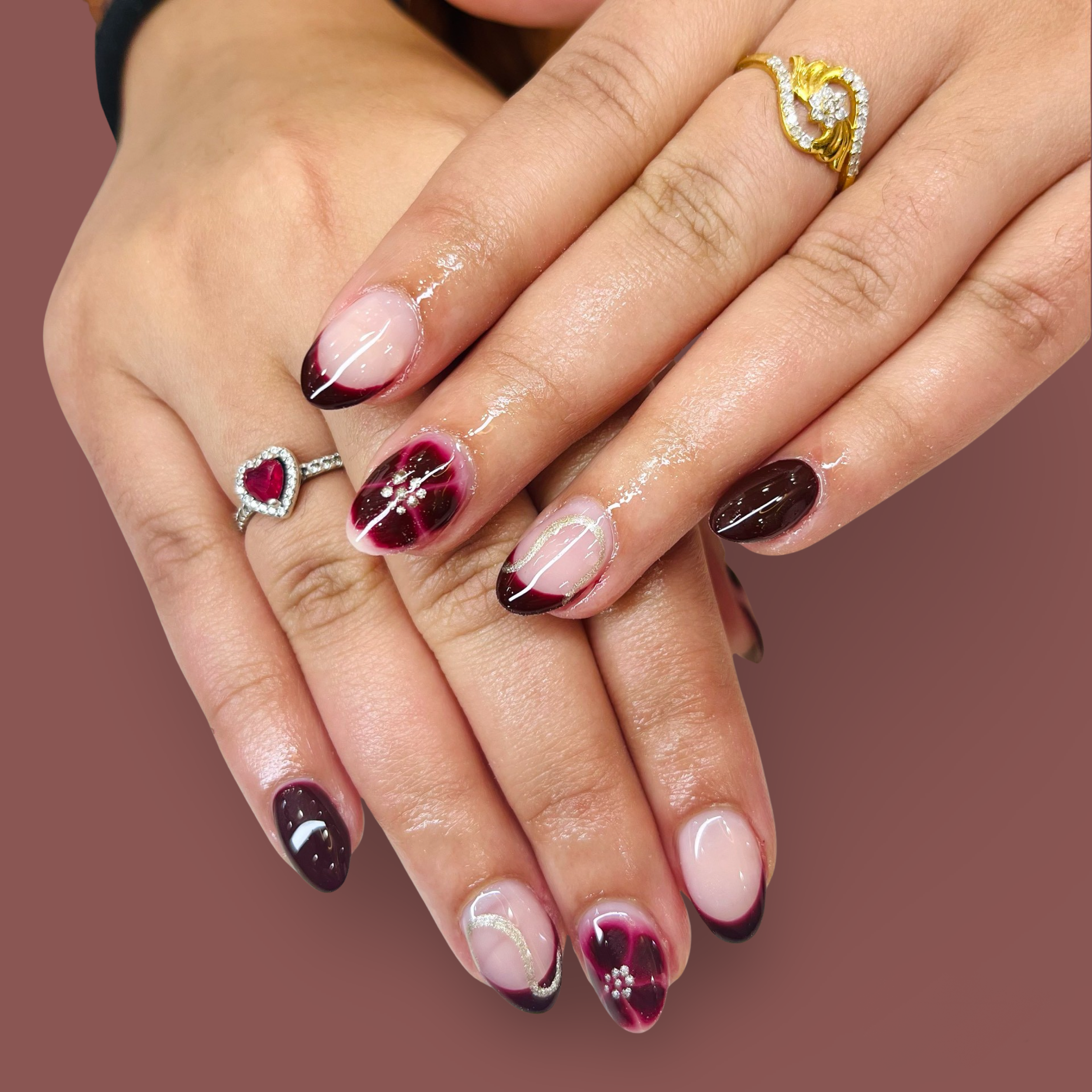 Close-up of hands with manicured nails featuring black, white, and red designs, decorated with rings and shiny polish.