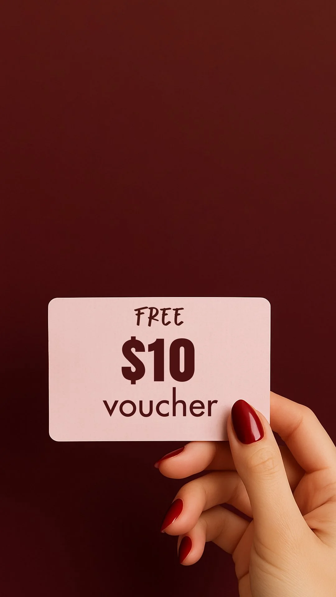 Hand with red painted nails holding a pink voucher card that says 'Free $10 voucher' against a dark maroon background.