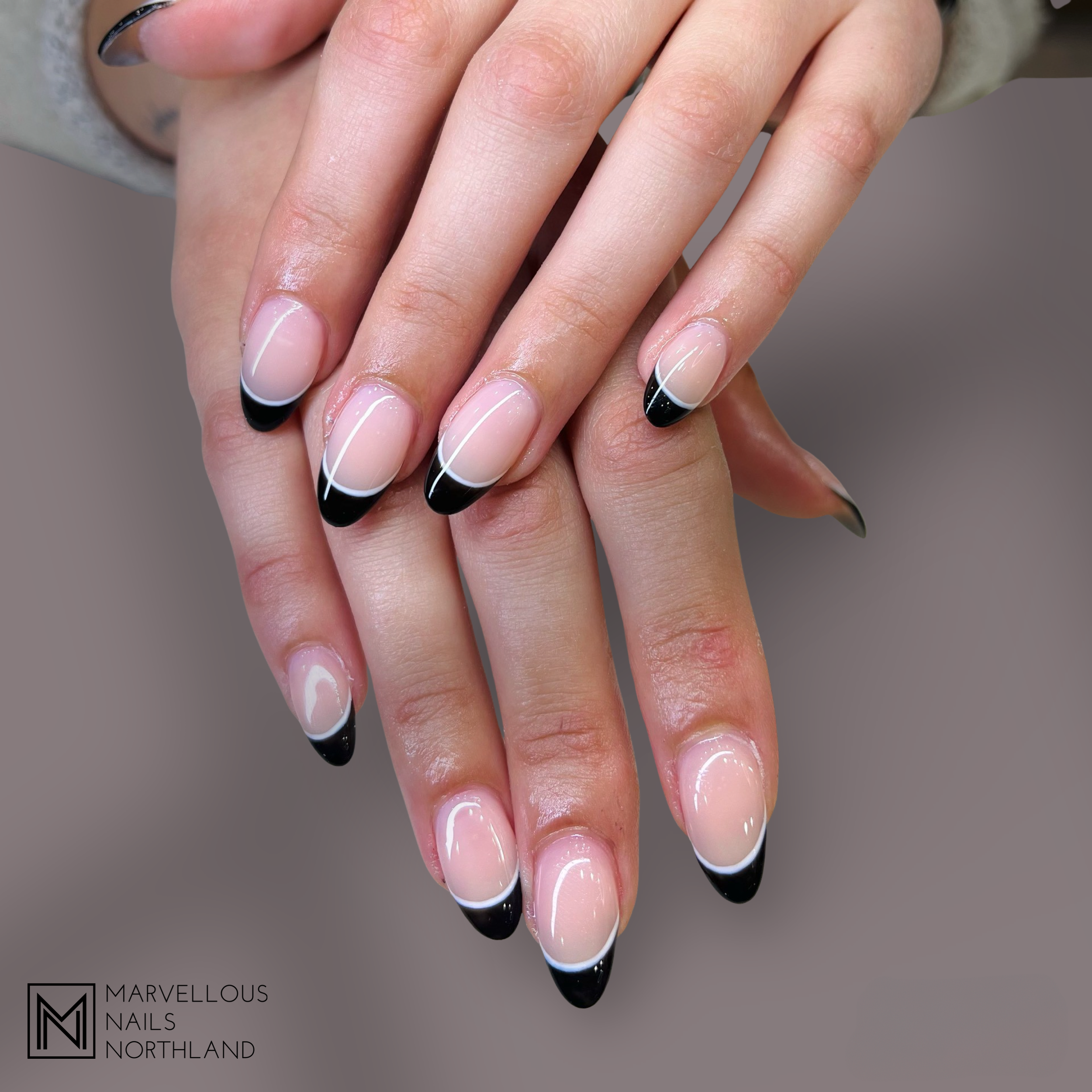 Close-up of hands with manicured nails painted in a black and white French tip style.