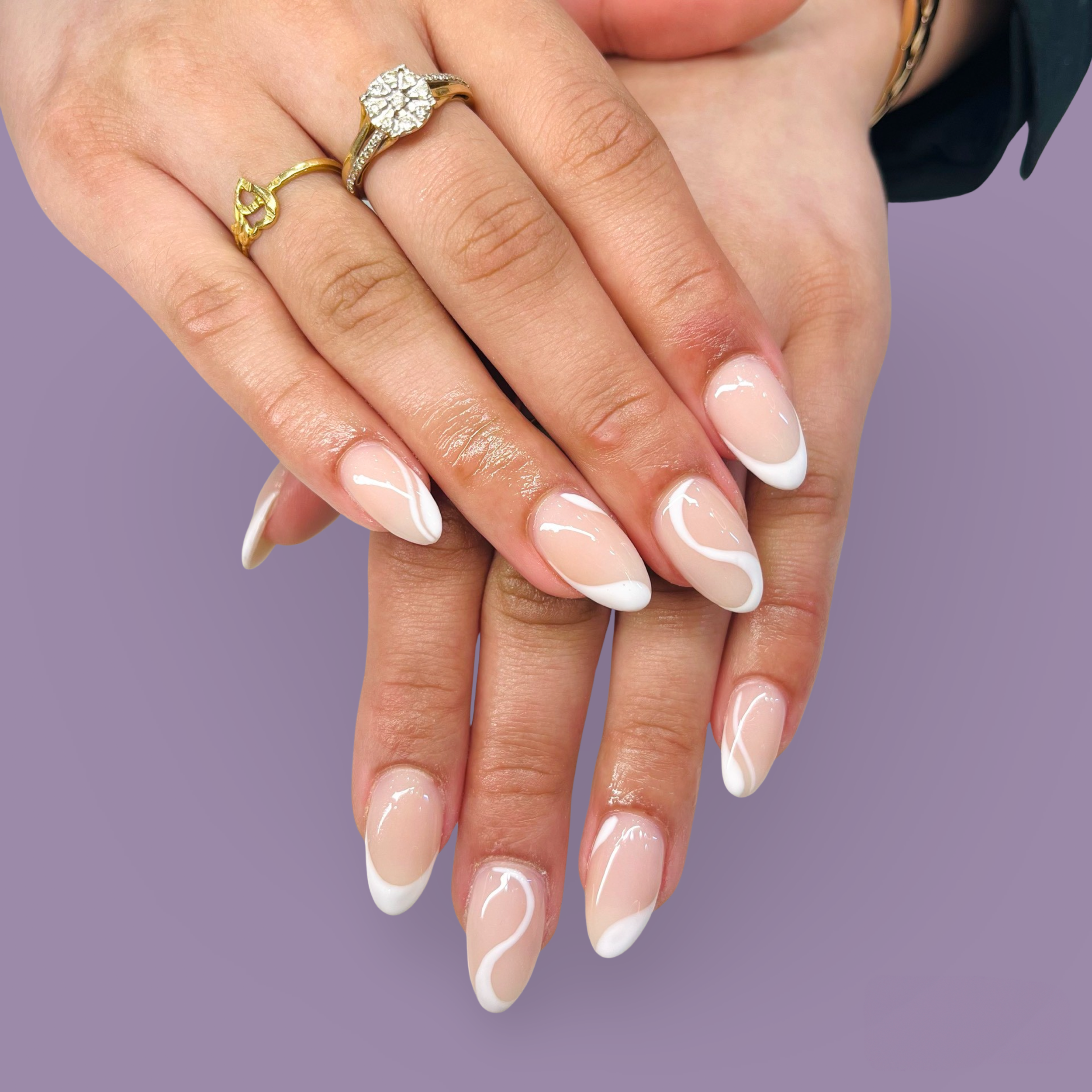 Close-up of a person's hands with white French manicure nails and gold rings, one with diamonds, against a purple background.