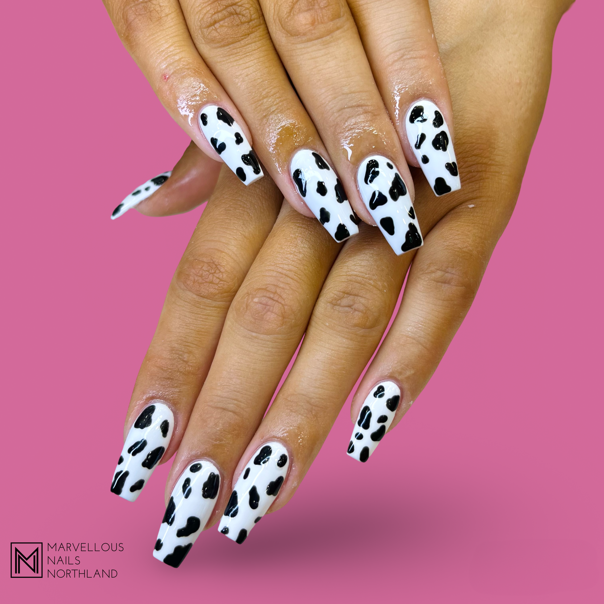Hand with long, square-shaped nails featuring a black-and-white leopard print design against a pink background.