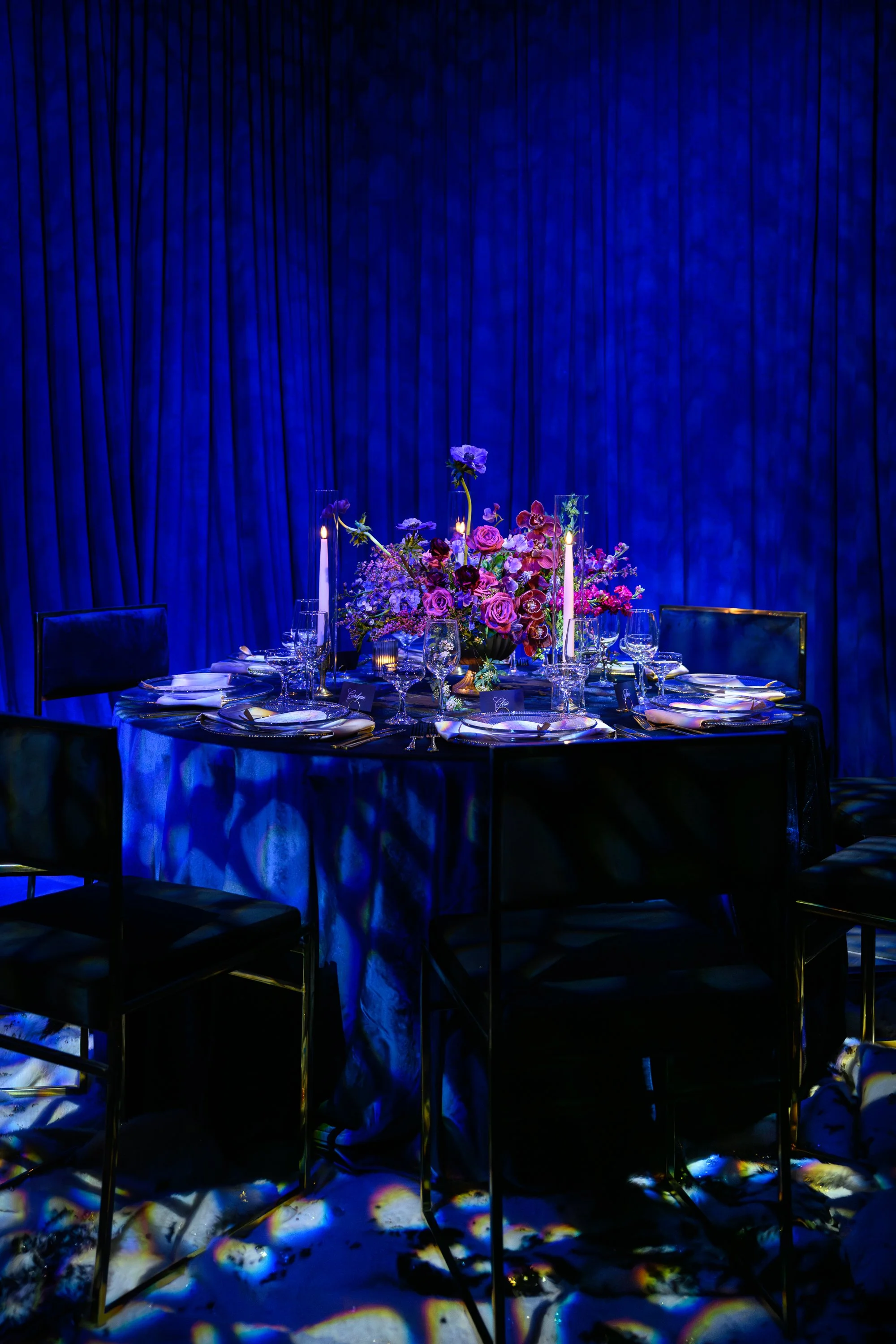 Decorated dining table with floral centerpiece, candles, and fine glassware, set against a dark blue curtain background. HSP event production in Boston MA