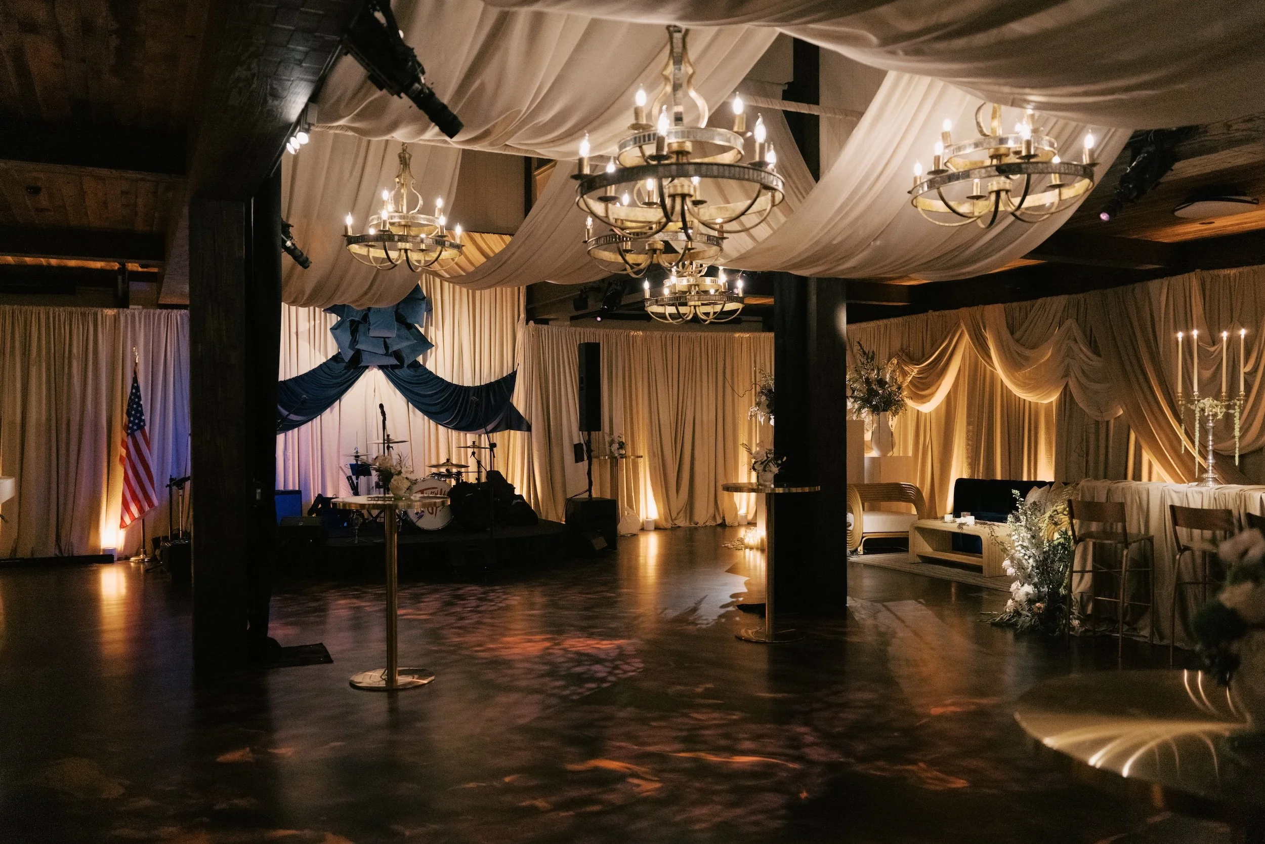 A decorated event hall with draped fabric on the ceiling, elegant chandeliers, and floral arrangements, set up for a celebration or wedding reception. HSP event production in Boston MA