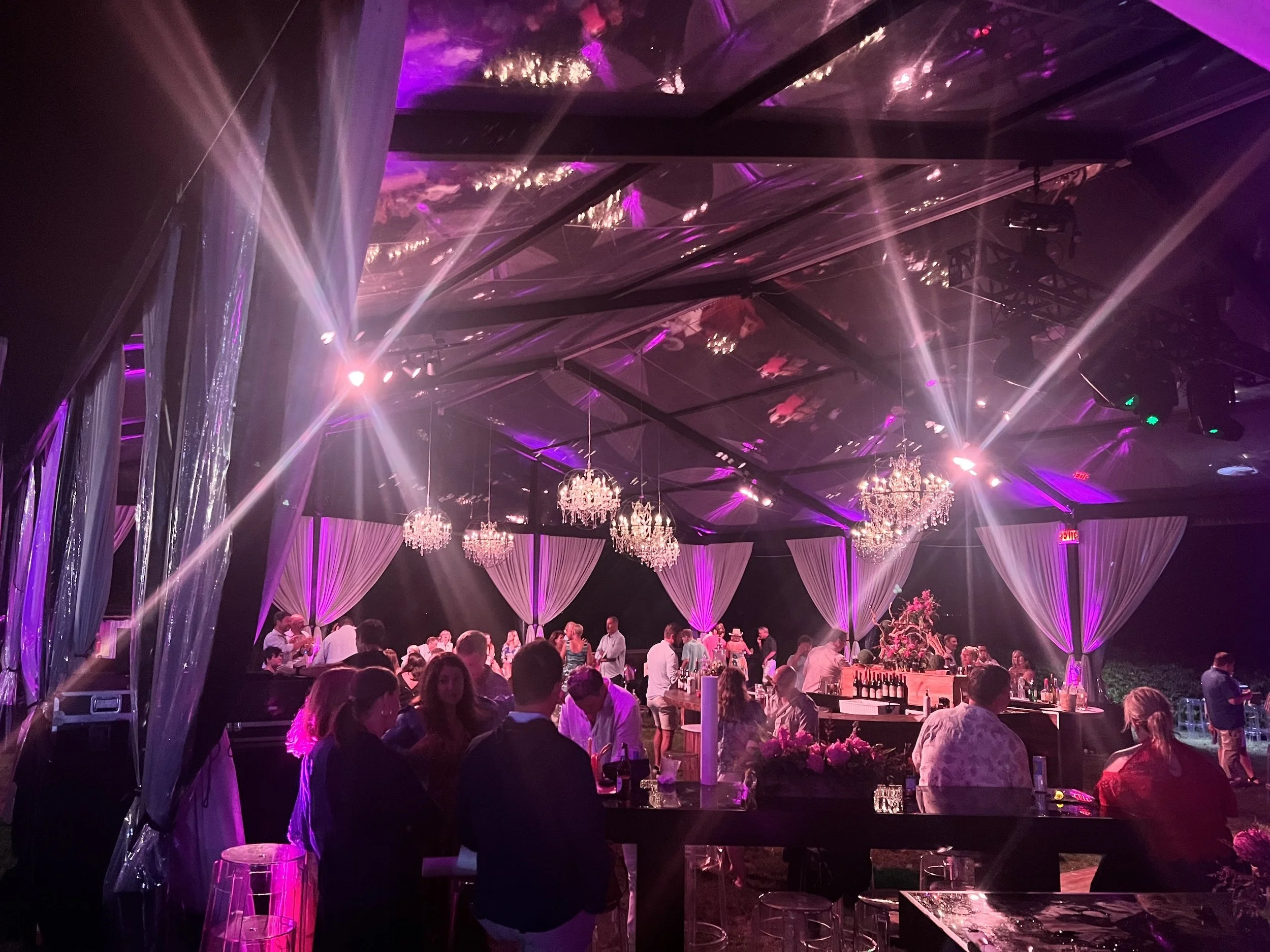 Party scene with people socializing in a decorated venue with purple lighting, chandeliers, and draped curtains. HSP event production in Boston MA