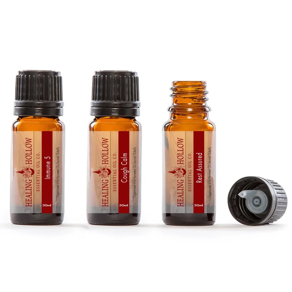 Three small amber glass bottles of Healing Hollow essential oil with labels indicating different blends, and one bottle cap lying nearby.
