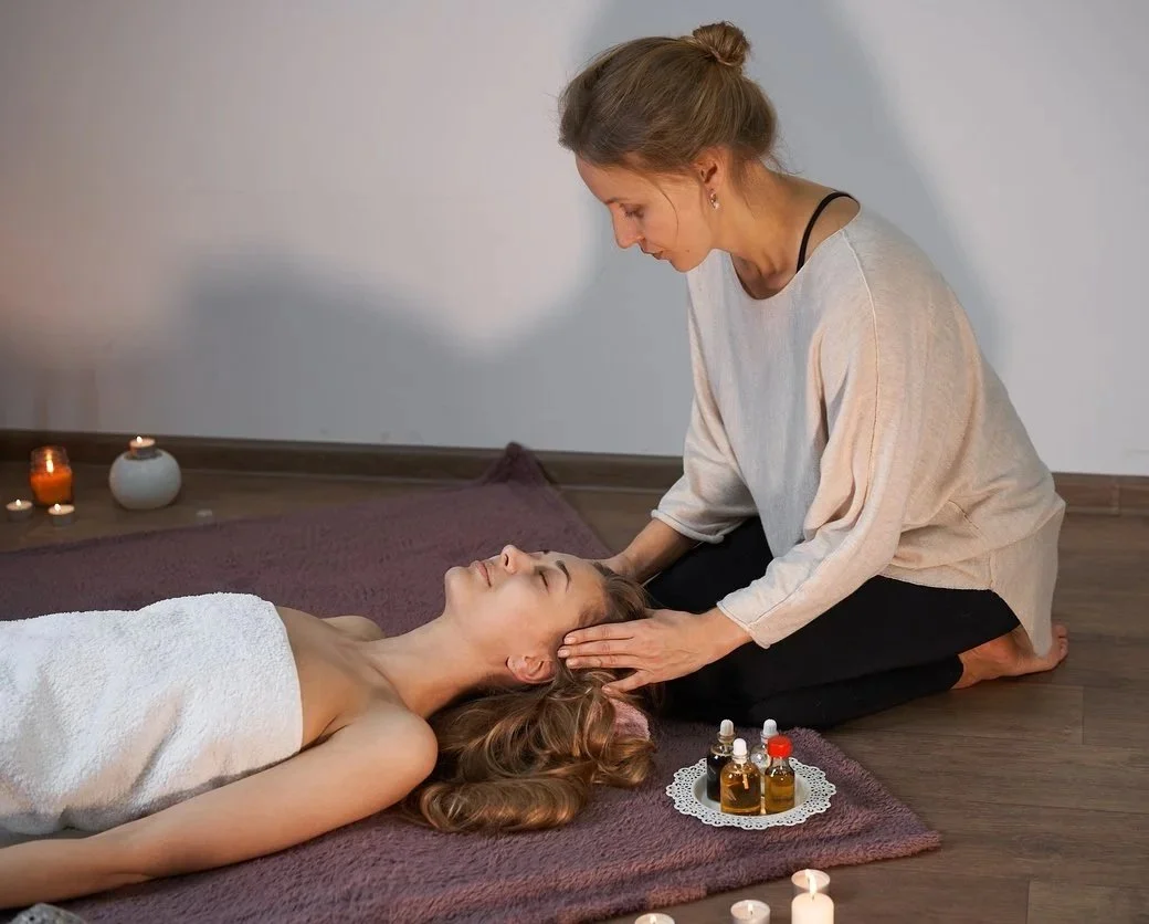 A woman receiving a head massage in a spa setting with candles and massage oils on a small tray nearby.