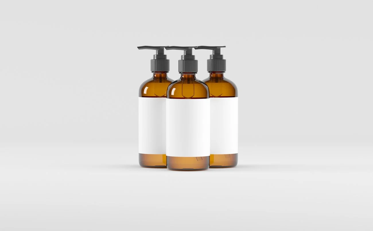 Three amber glass bottles with pump dispensers and blank white labels, arranged in a row on a white background.